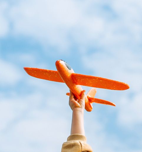 A child's hand holding a toy airplane up to the sky