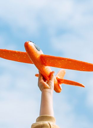 A child's hand holding a toy airplane up to the sky