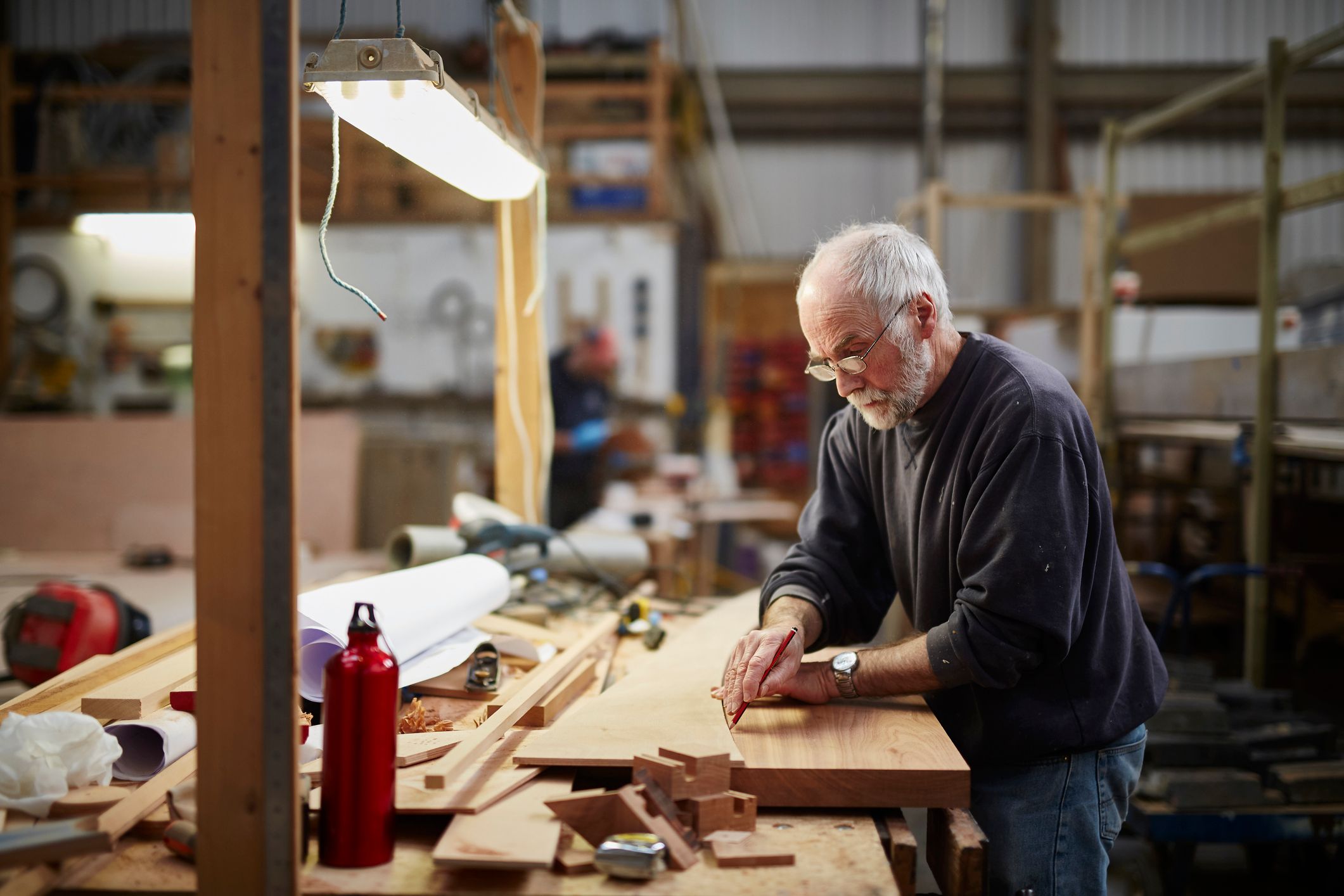 A late-middle aged man in a woodworking shop, measuring out a design.