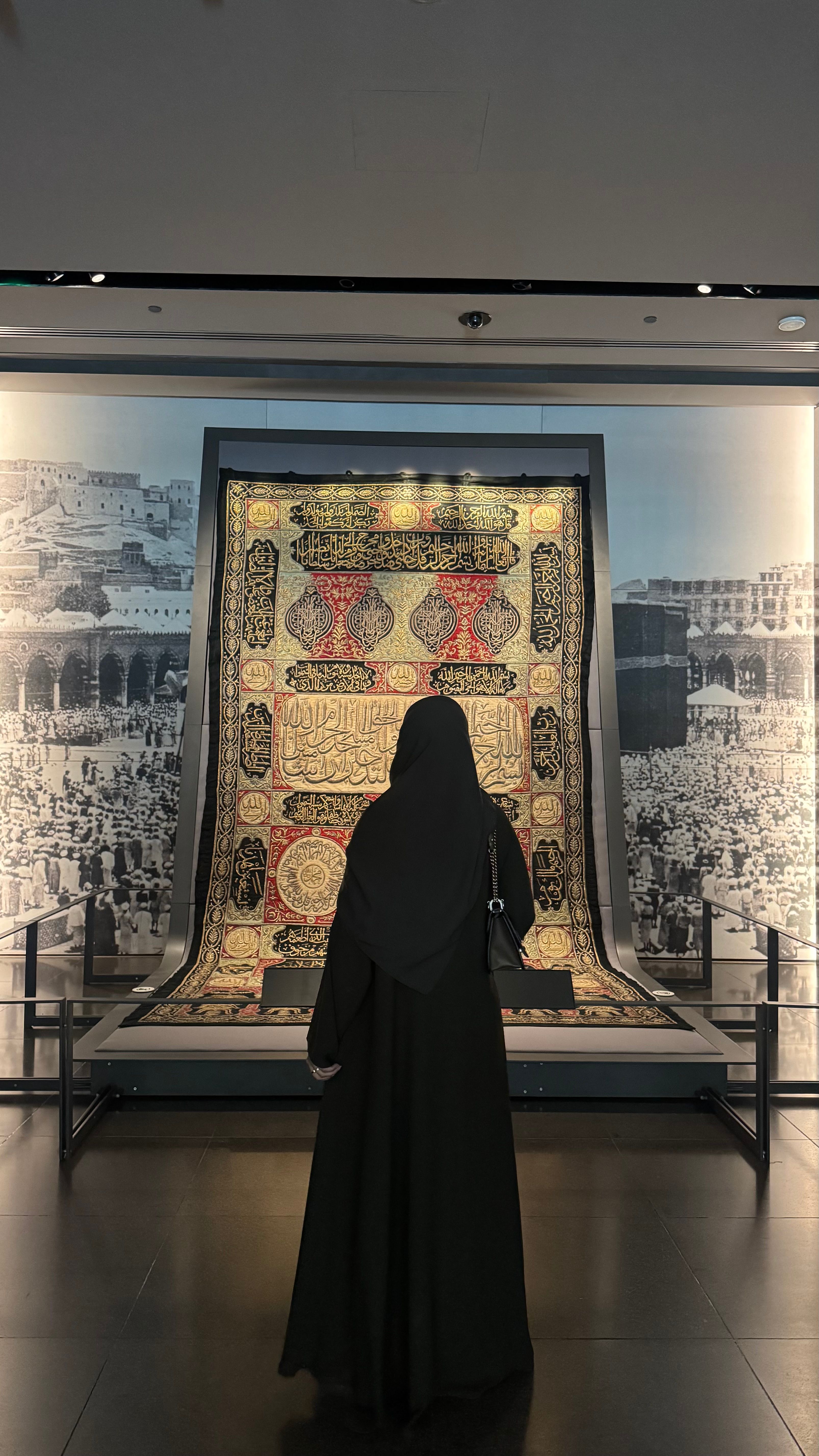 الفنانة من الخلف، تتأمل نسيجاً مطرّزاً في قاعة متحف