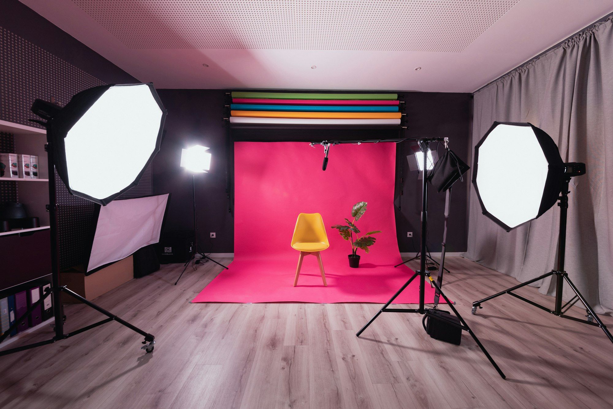 A photography studio with a pink paper backdrop, two softboxes on stands and a yellow chair