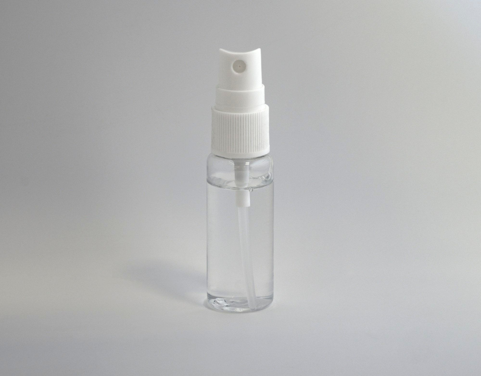 A clear plastic spray bottle containing a transparent liquid, photographed against a plain grey background