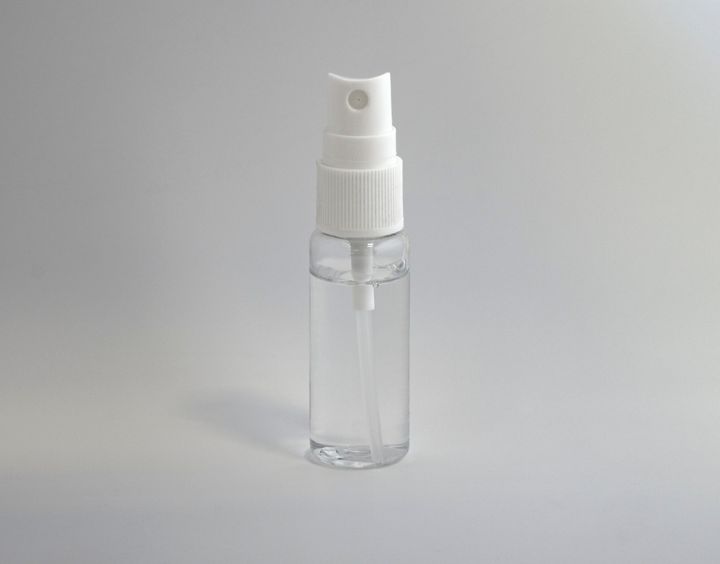 A clear plastic spray bottle containing a transparent liquid, photographed against a plain grey background