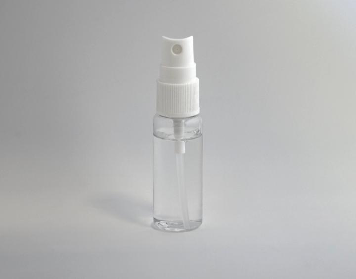 A clear plastic spray bottle containing a transparent liquid, photographed against a plain grey background