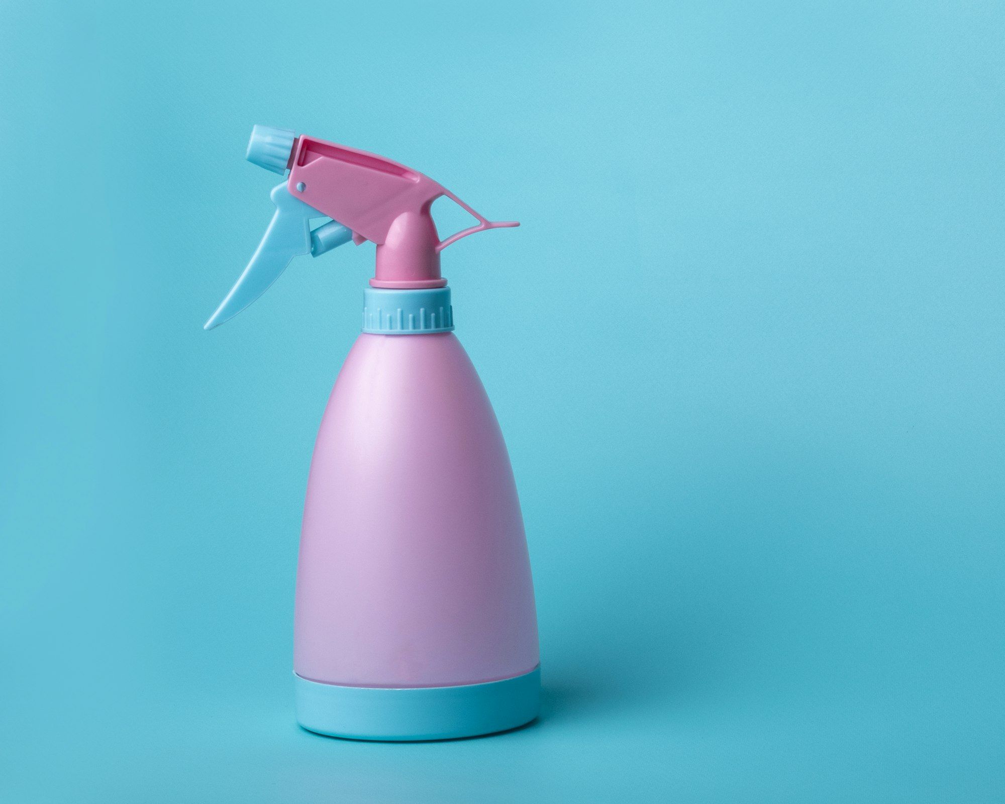 A pink and pale blue trigger spray bottle photographed against a plain blue background