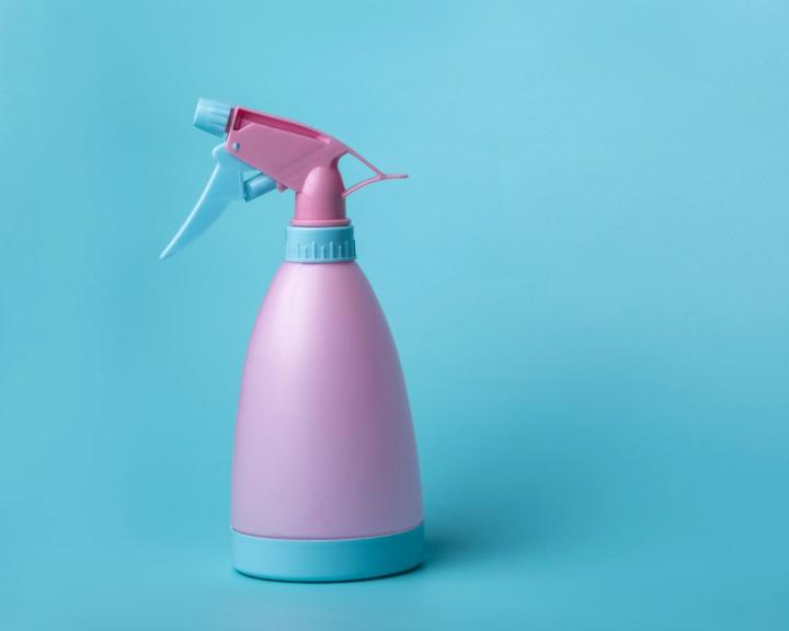 A pink and pale blue trigger spray bottle photographed against a plain blue background