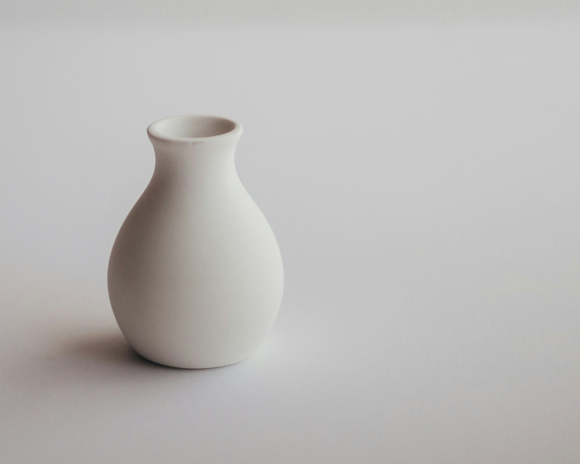 A white ceramic vase on a white surface, showing a soft contact shadow at its base and a single light direction.
