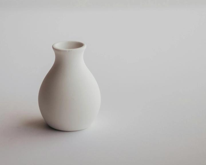 A white ceramic vase on a white surface, showing a soft contact shadow at its base and a single light direction.