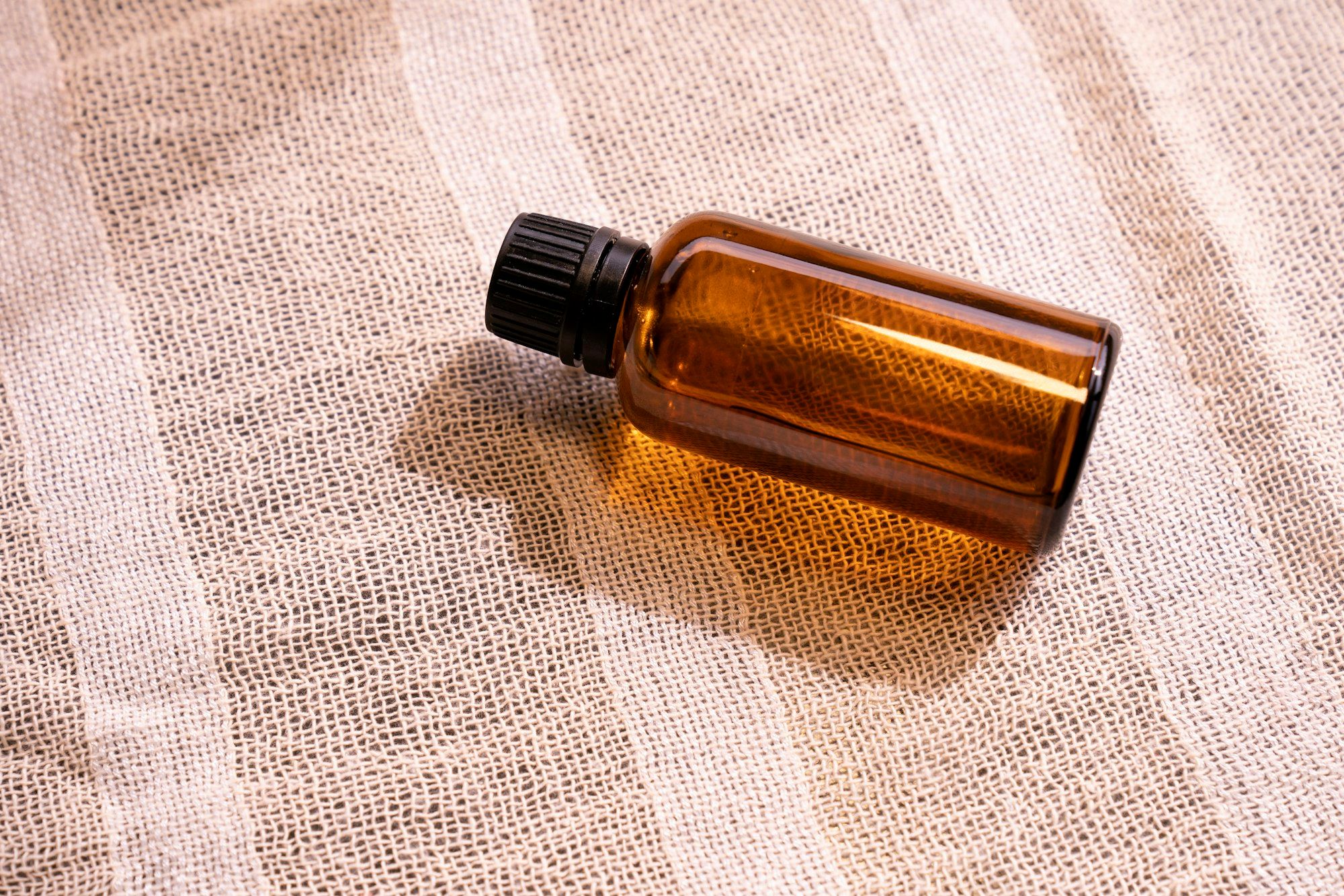An unbranded amber glass bottle with a black ribbed cap, backlit on a linen surface