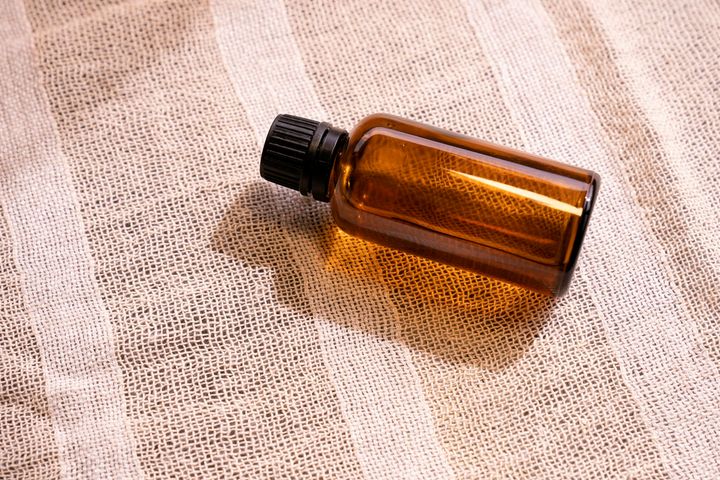 An unbranded amber glass bottle with a black ribbed cap, backlit on a linen surface