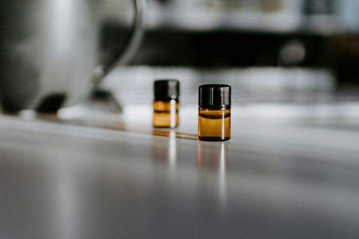Two small amber glass vials with black caps on a reflective grey surface, each throwing a highlight and a soft reflection