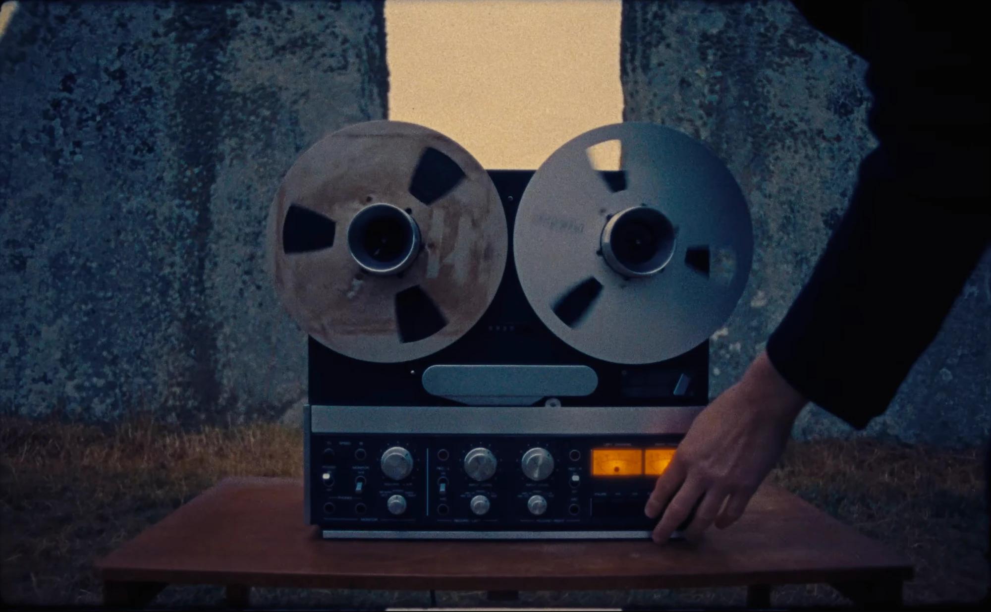 A reel-to-reel tape machine on a wooden table between the standing stones at Stonehenge at dusk