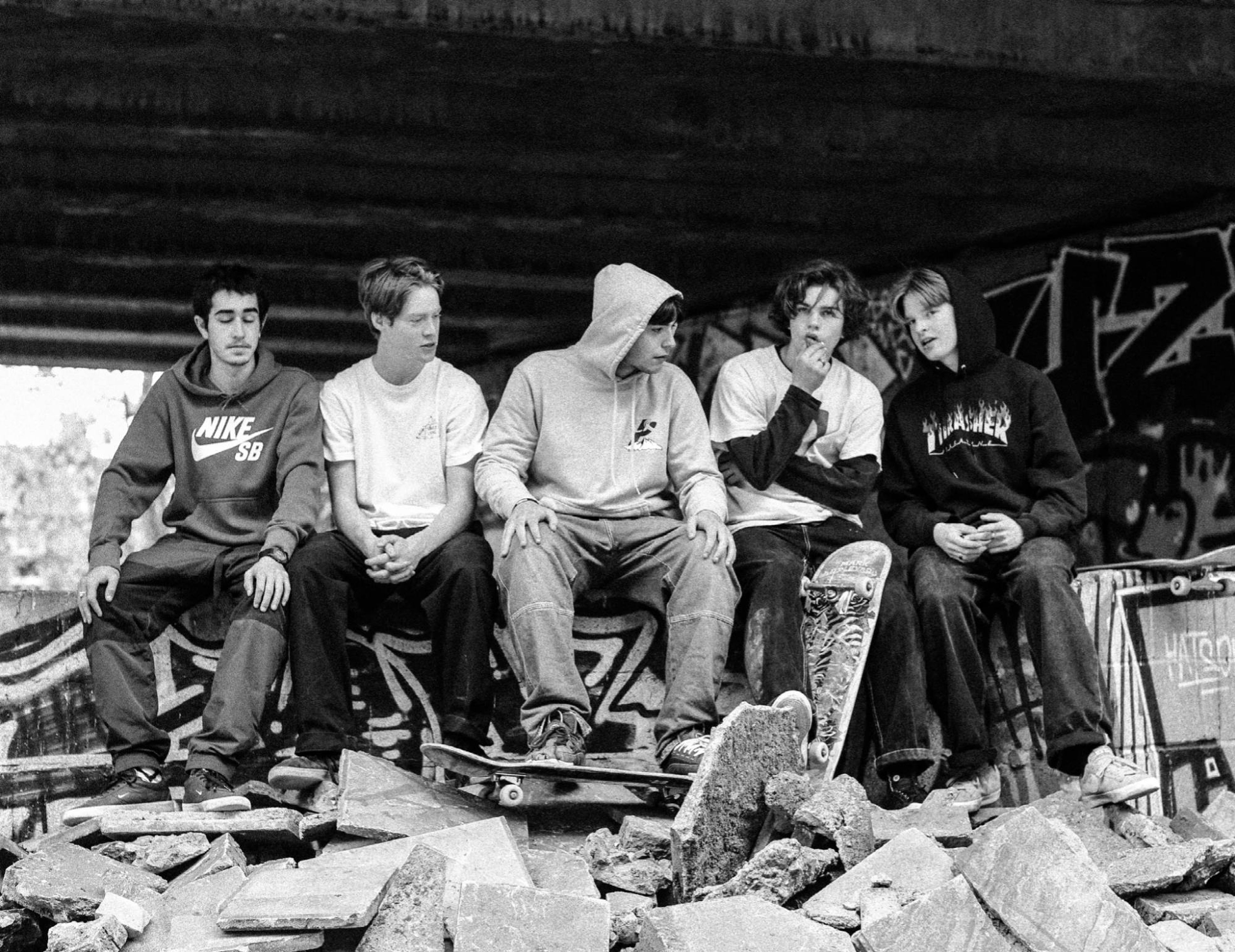 Five skaters sitting on rubble under a flyover