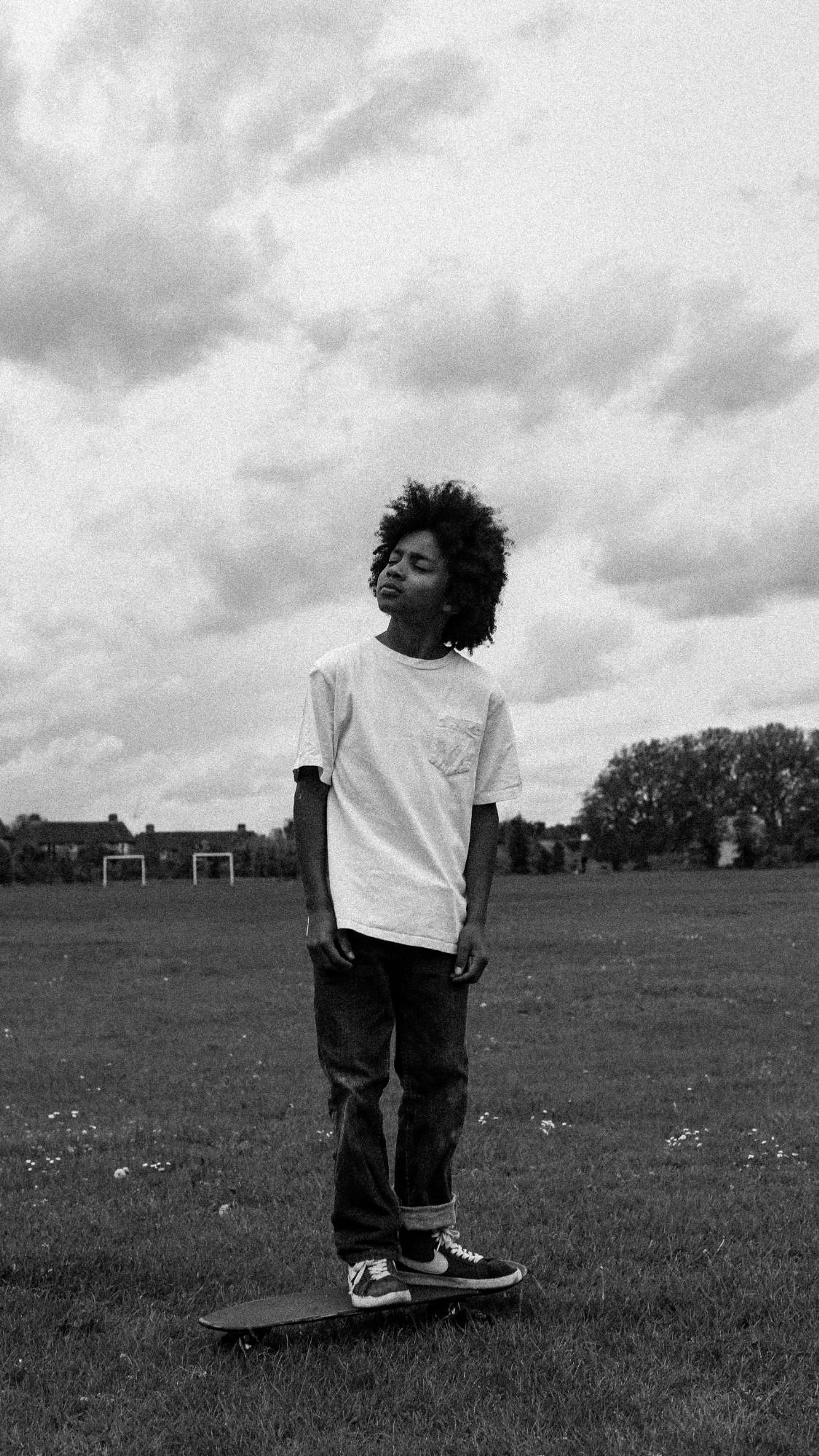 A boy standing on a skateboard in a park under a cloudy sky