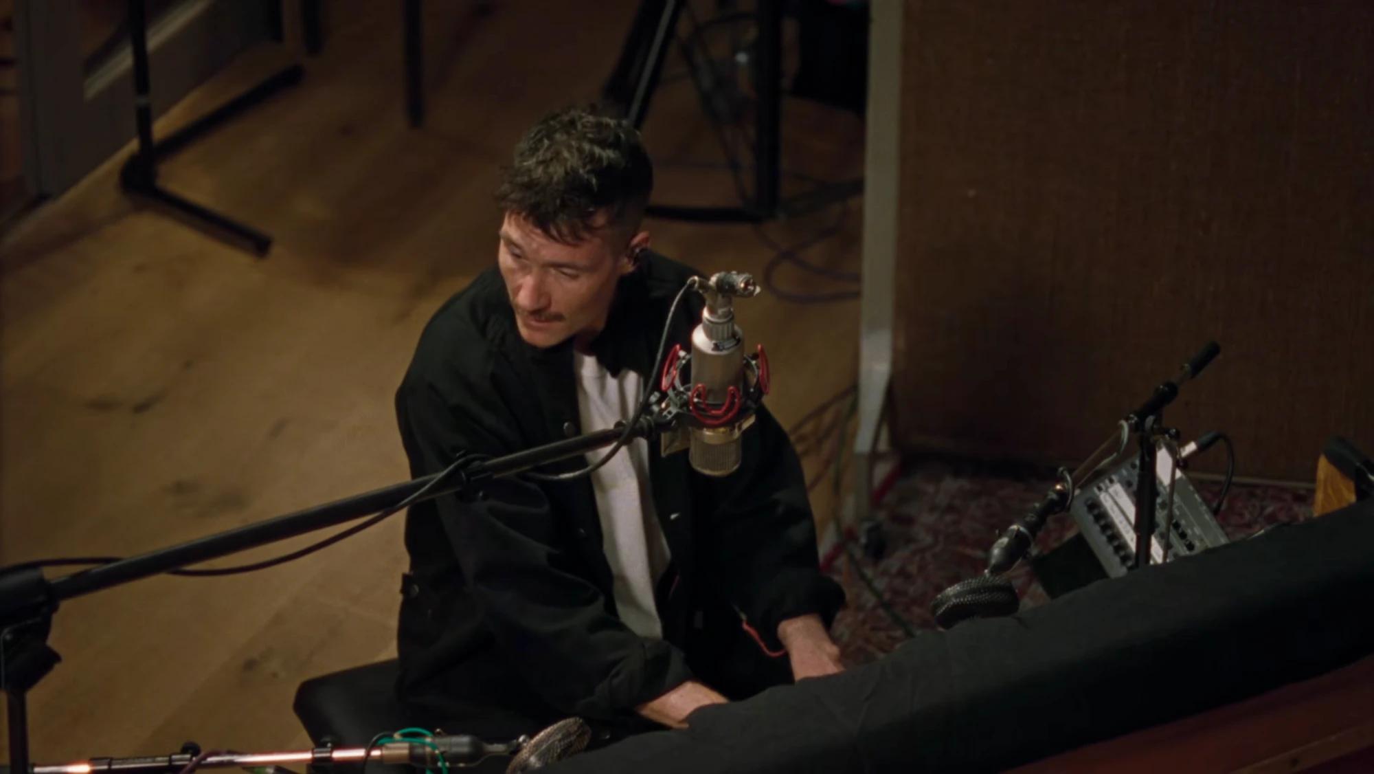 A singer in a black jacket at the piano, seen from above, surrounded by microphones in the Abbey Road studio