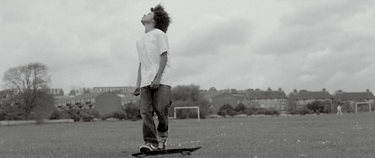 A boy on a skateboard in a park, looking up at the sky