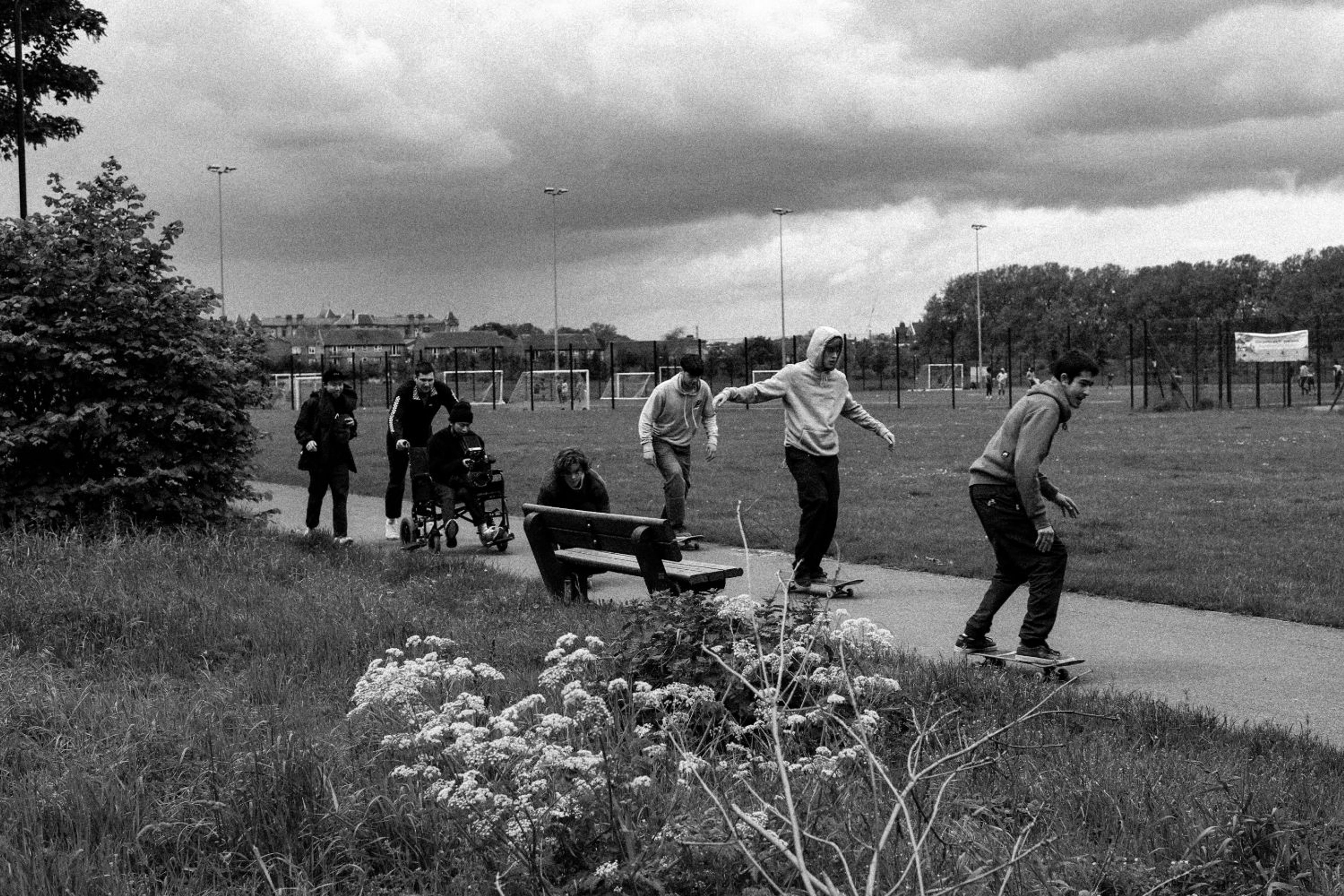 Skaters riding along a park path as the crew follows with a camera in a wheelchair