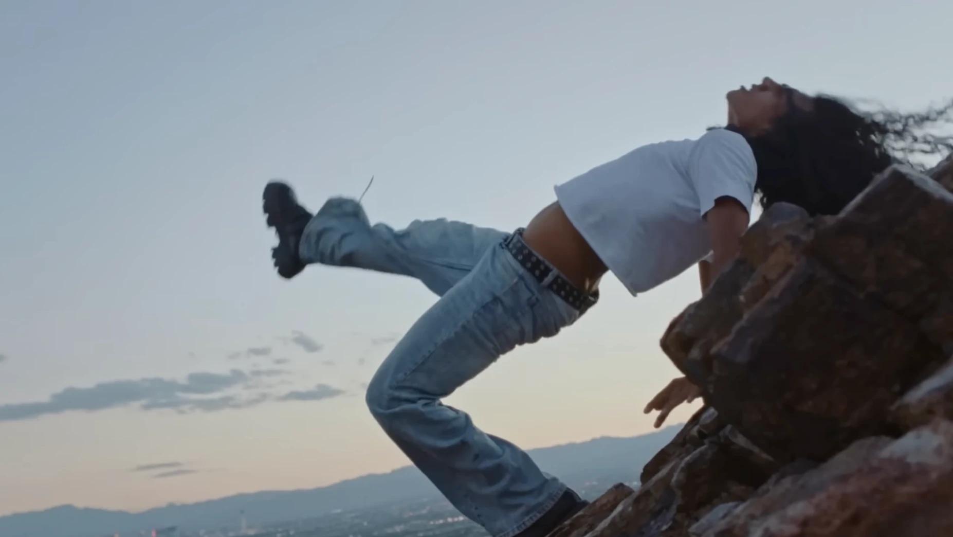 A dancer in jeans and a white T-shirt arches backwards against a rock face above Las Vegas at dusk