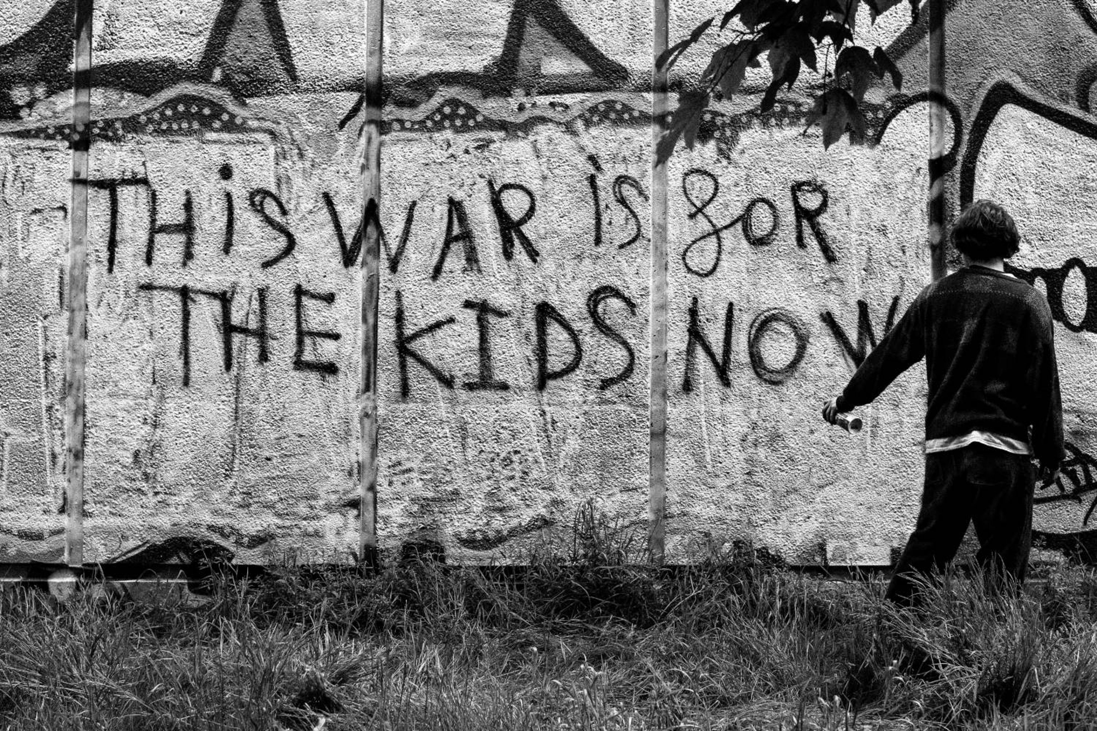 A boy beside graffiti reading This War Is For The Kids Now