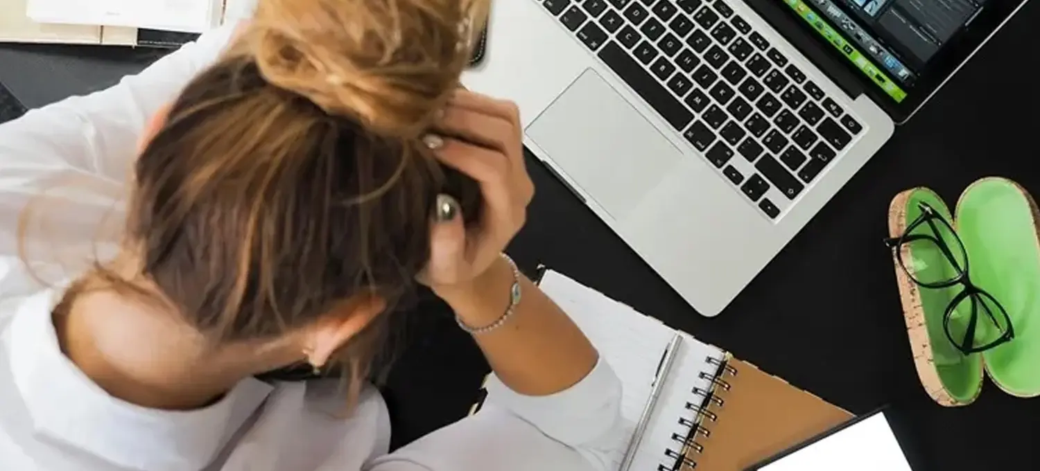 Professional woman in front of laptop with head in hands