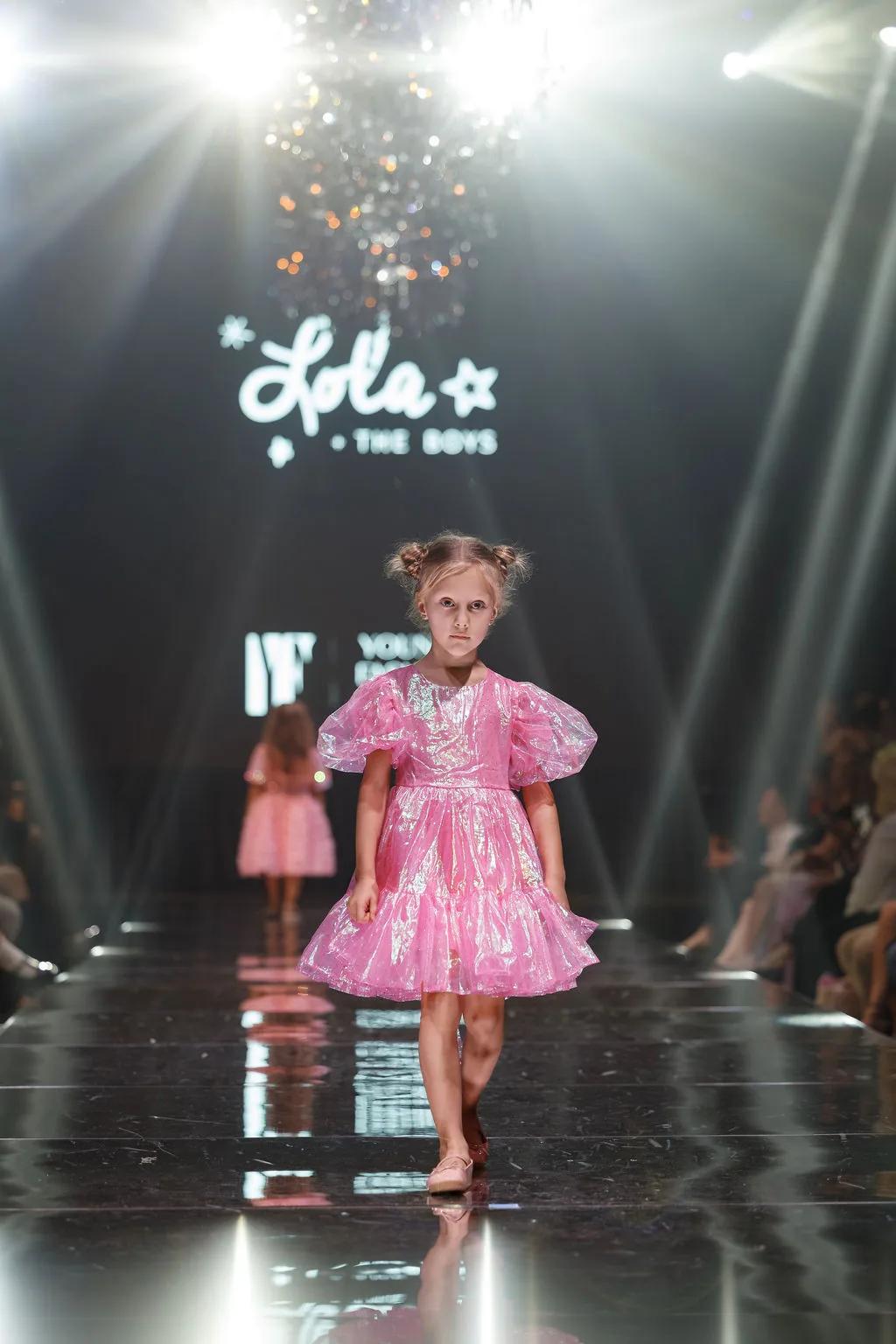 A girl in pink Lola + The Boys on the YFS runway, the brand on the screen behind