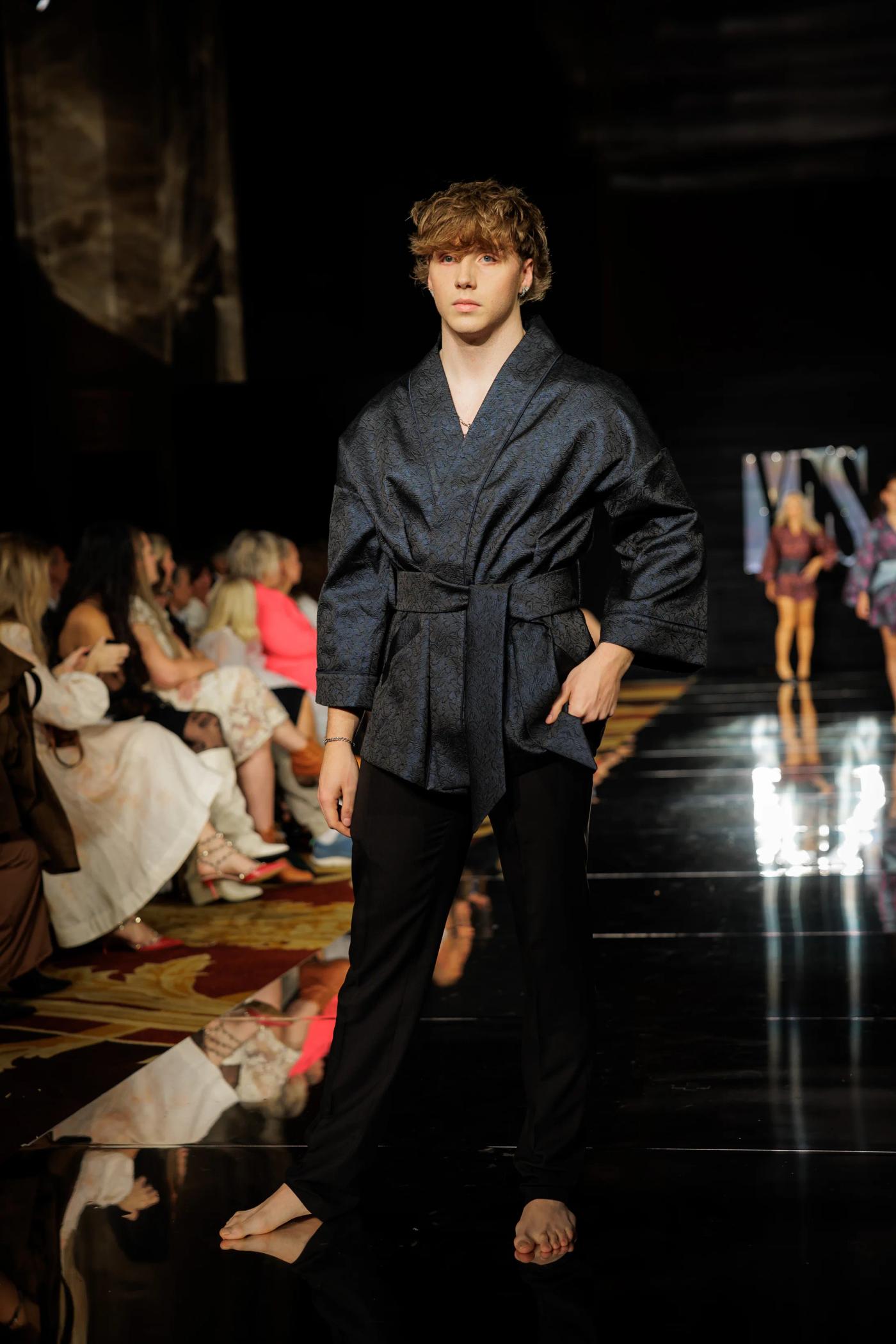 A male model in a dark belted jacket on the YFS runway