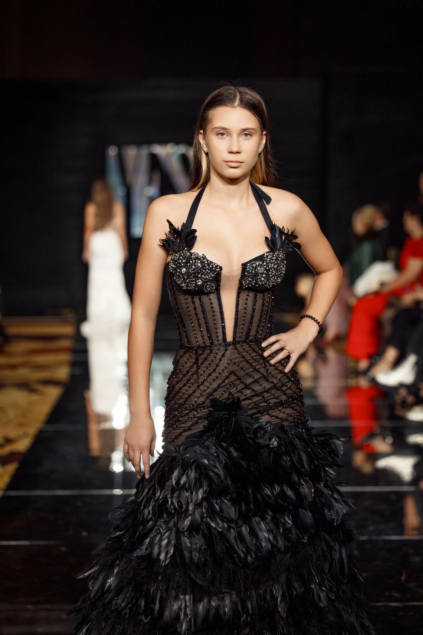 A model in a black feathered corset gown on the YFS runway