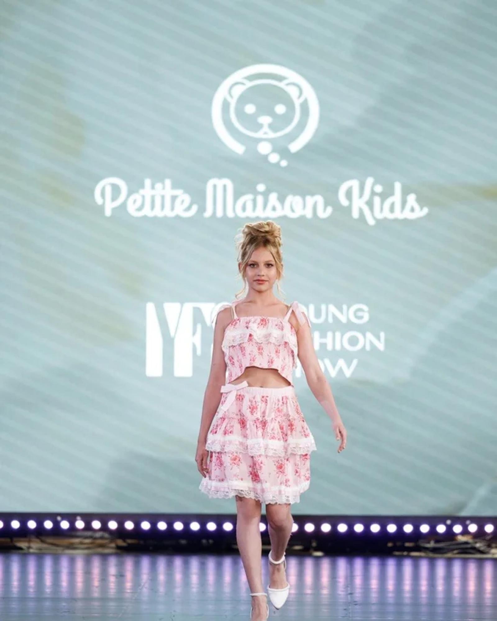 A young model in Petite Maison Kids on the YFS runway, the brand name on the screen behind