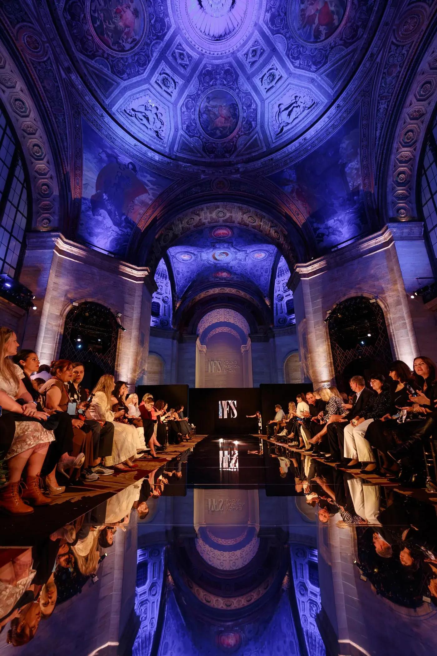 A full audience on both sides of a YFS runway in a vaulted, gilded hall