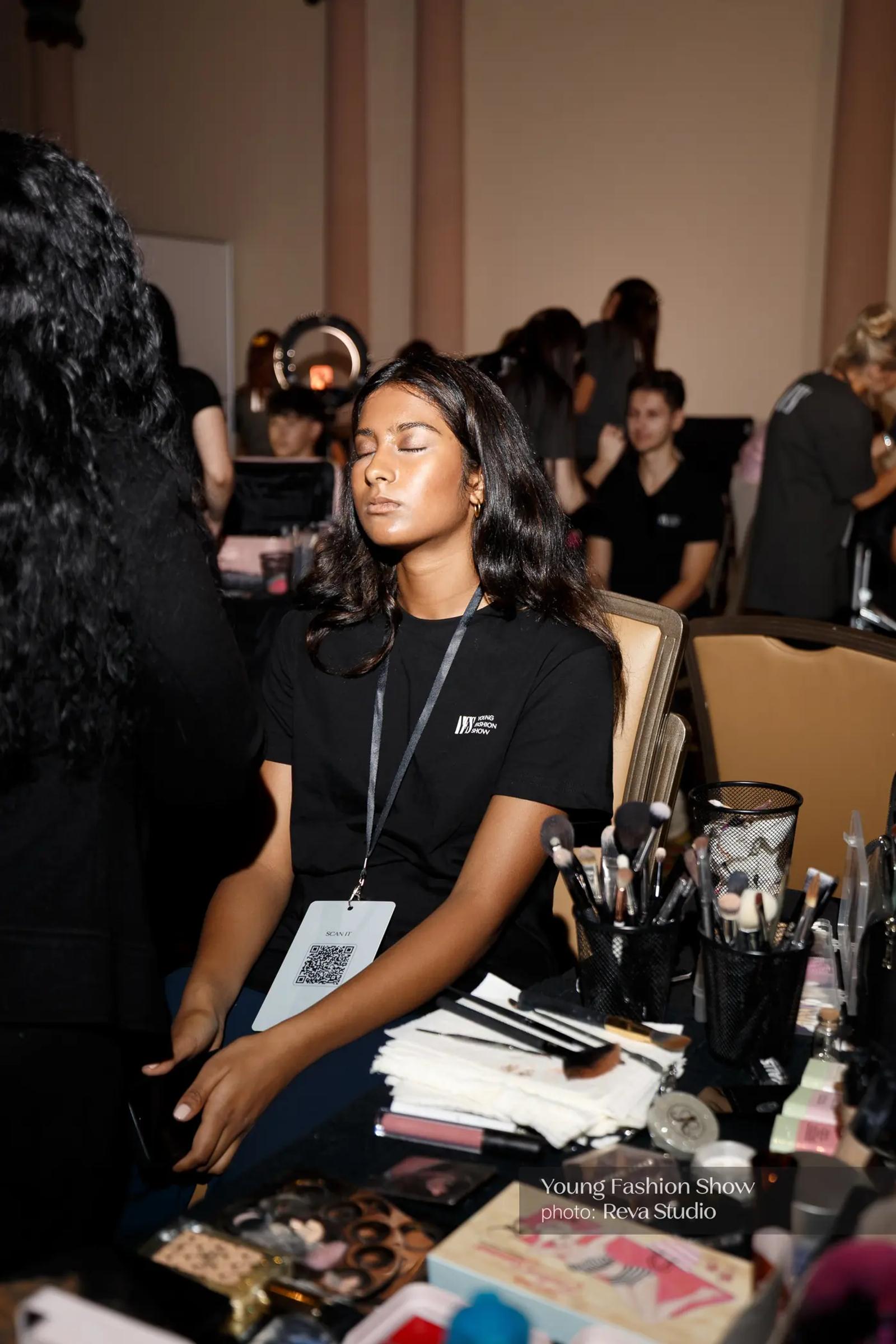 Participant seated at a backstage beauty station