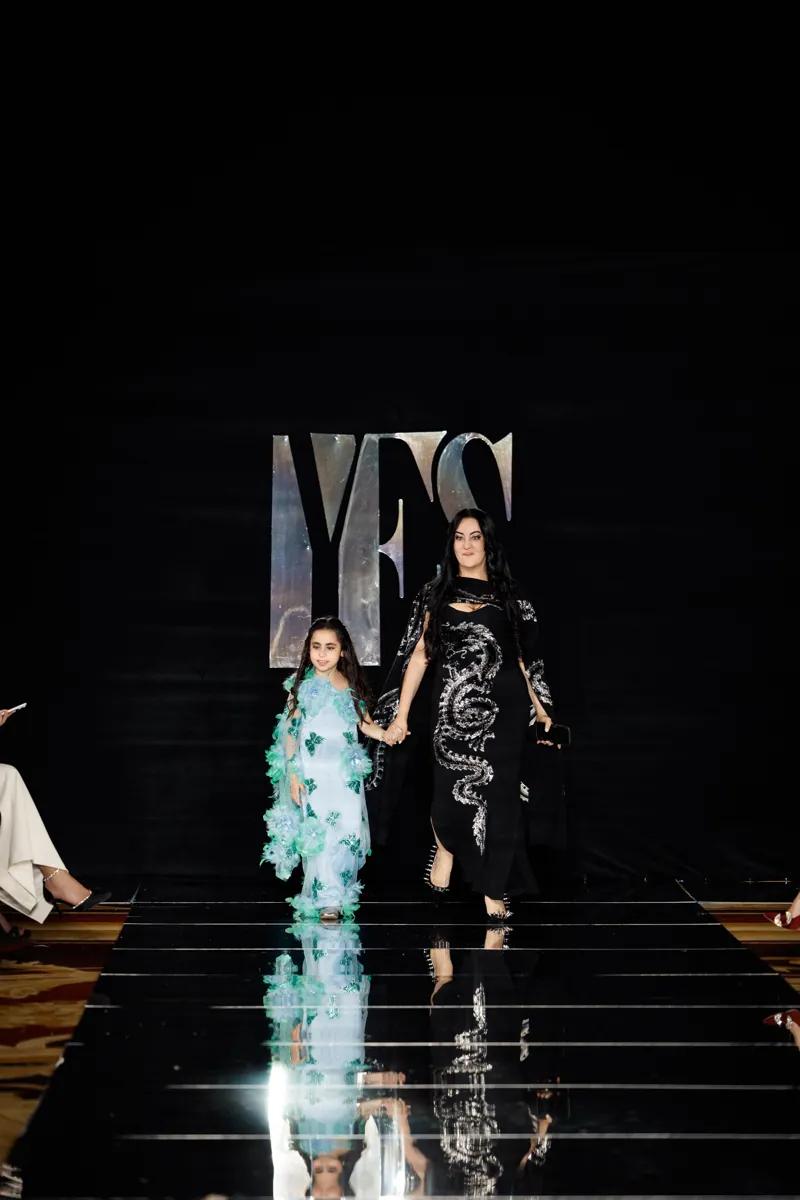 Layla Loren, founder of Milana Loren Couture, on the YFS runway with a model in a turquoise feathered gown