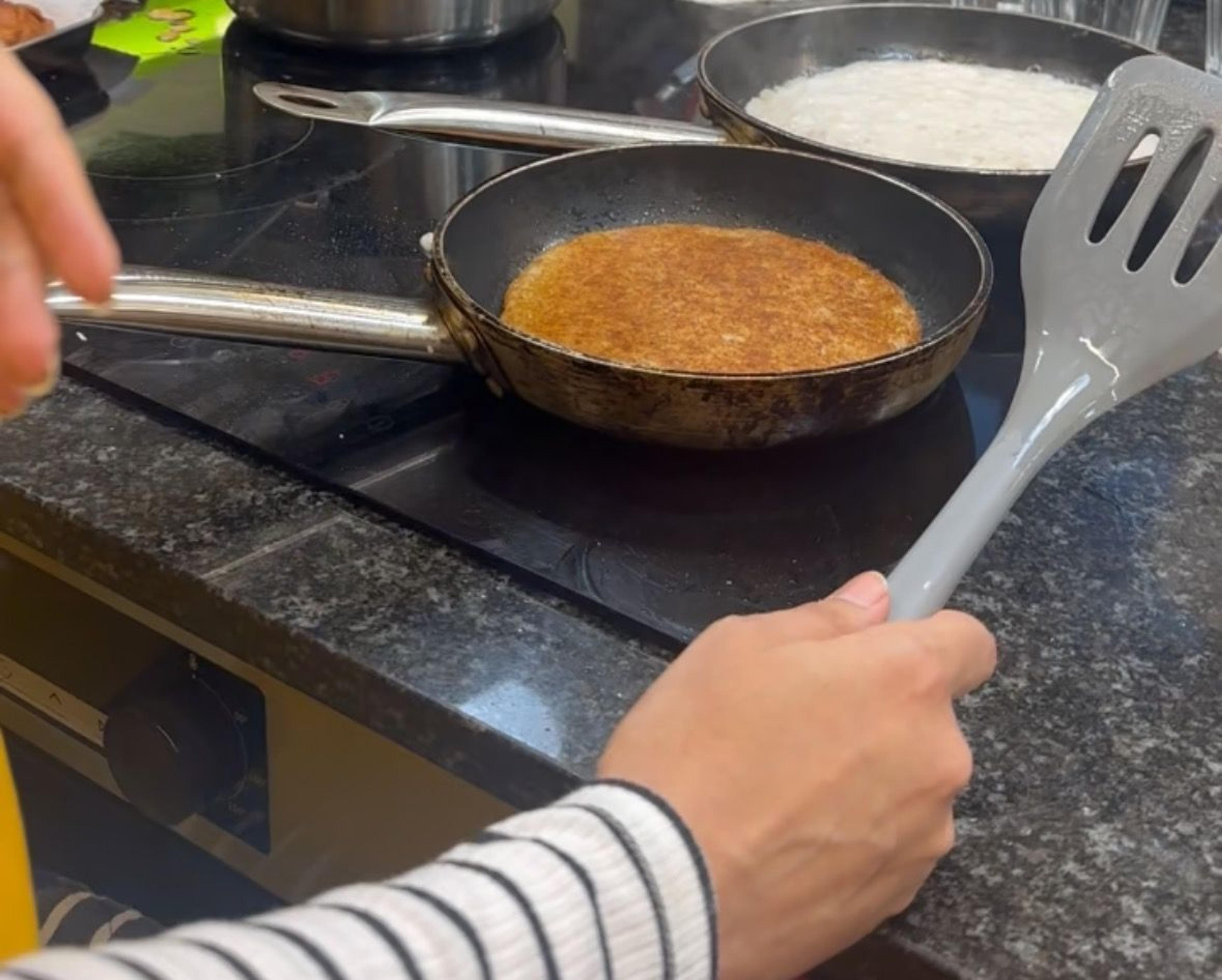 Hands frying a golden flatbread in a pan on the hob during a cooking class