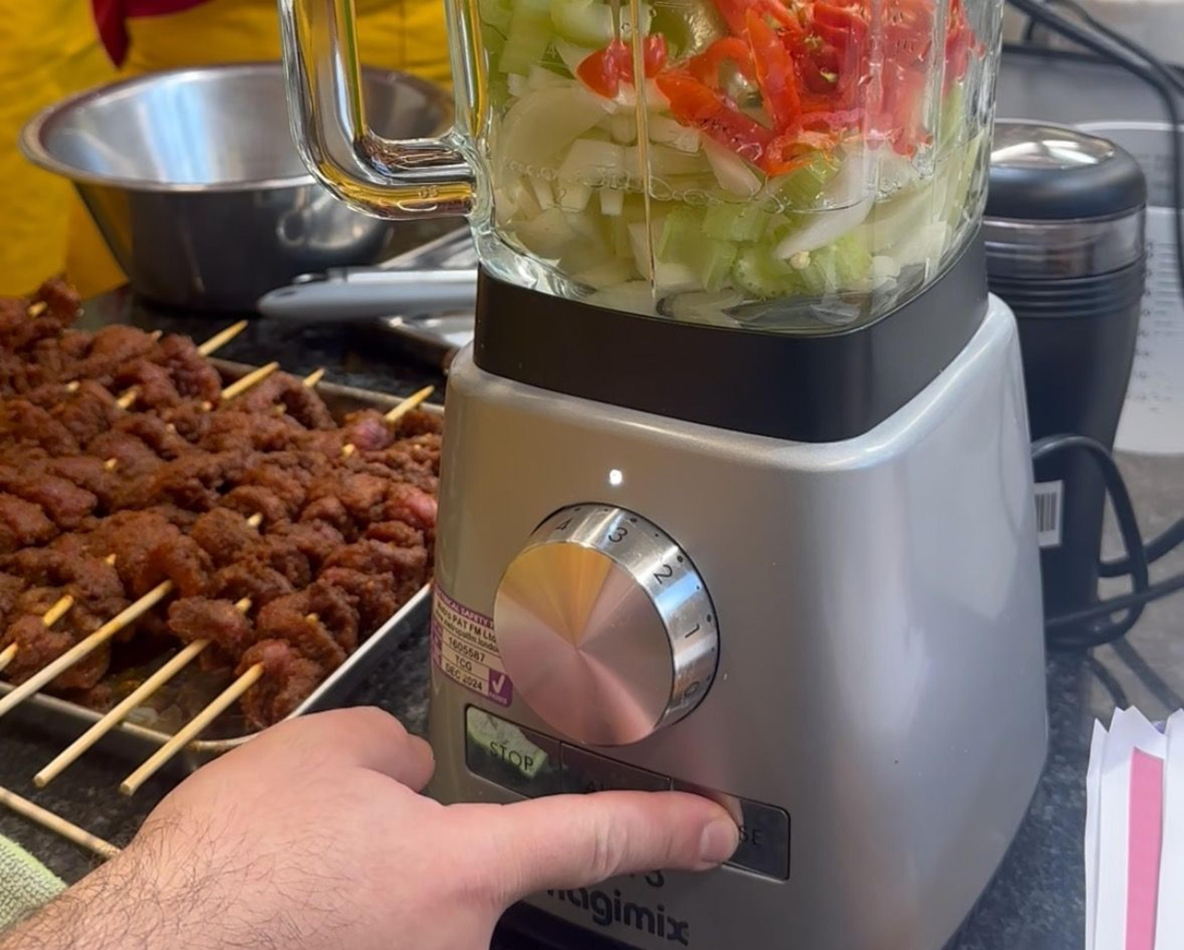 Blender of chopped peppers and onions beside skewers of grilled suya at a cooking class