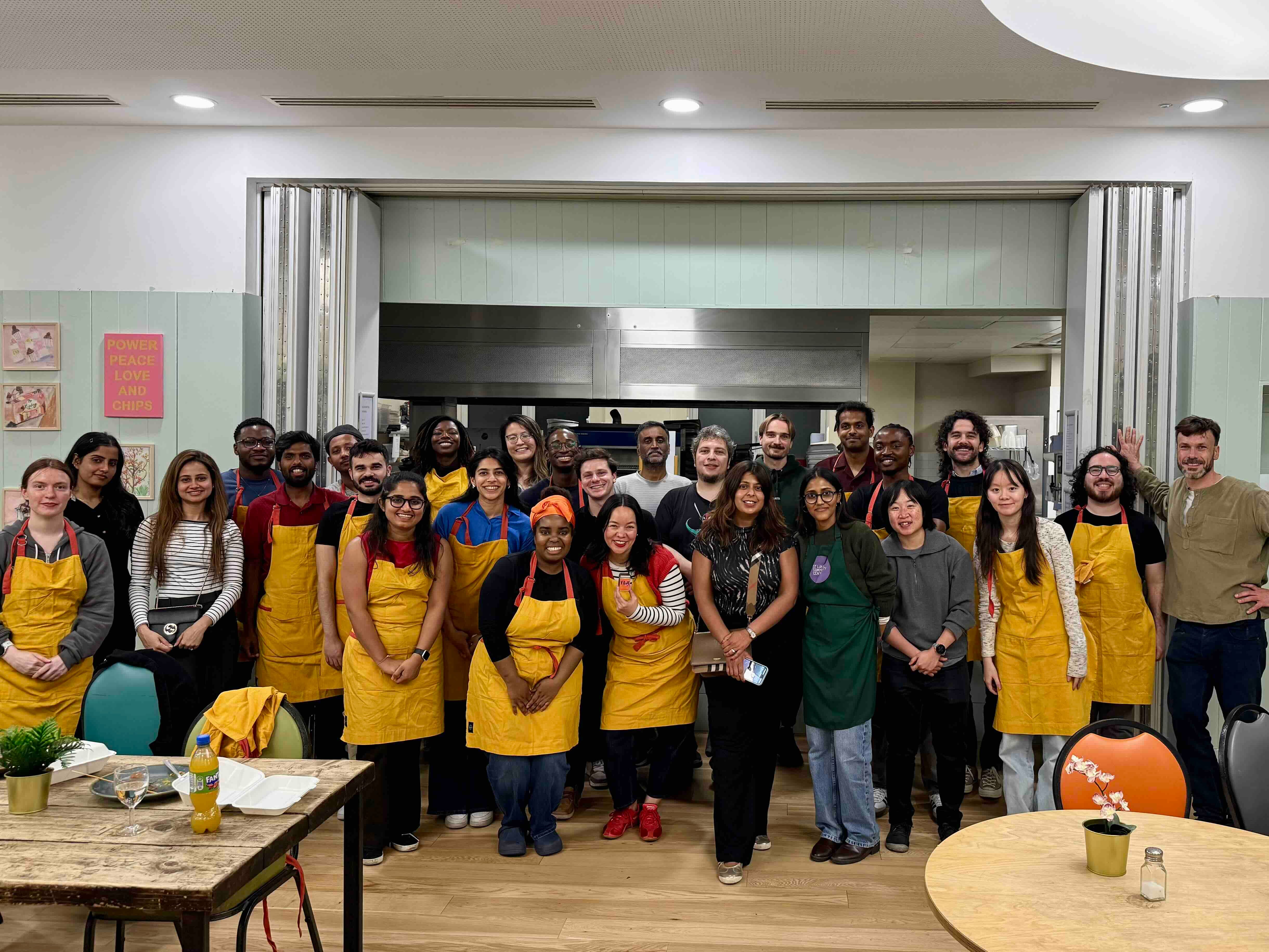 Large group of corporate cooking-class guests in aprons smiling together in the school kitchen