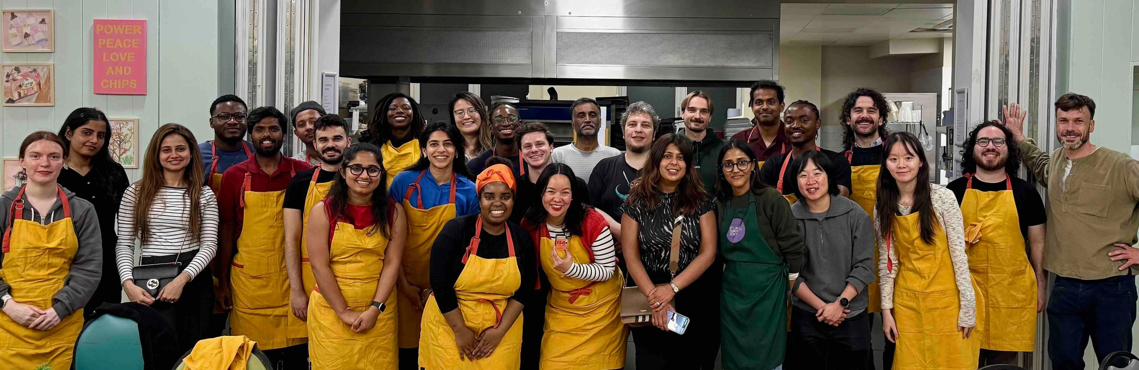 Large group of corporate cooking-class guests in aprons smiling together in the school kitchen