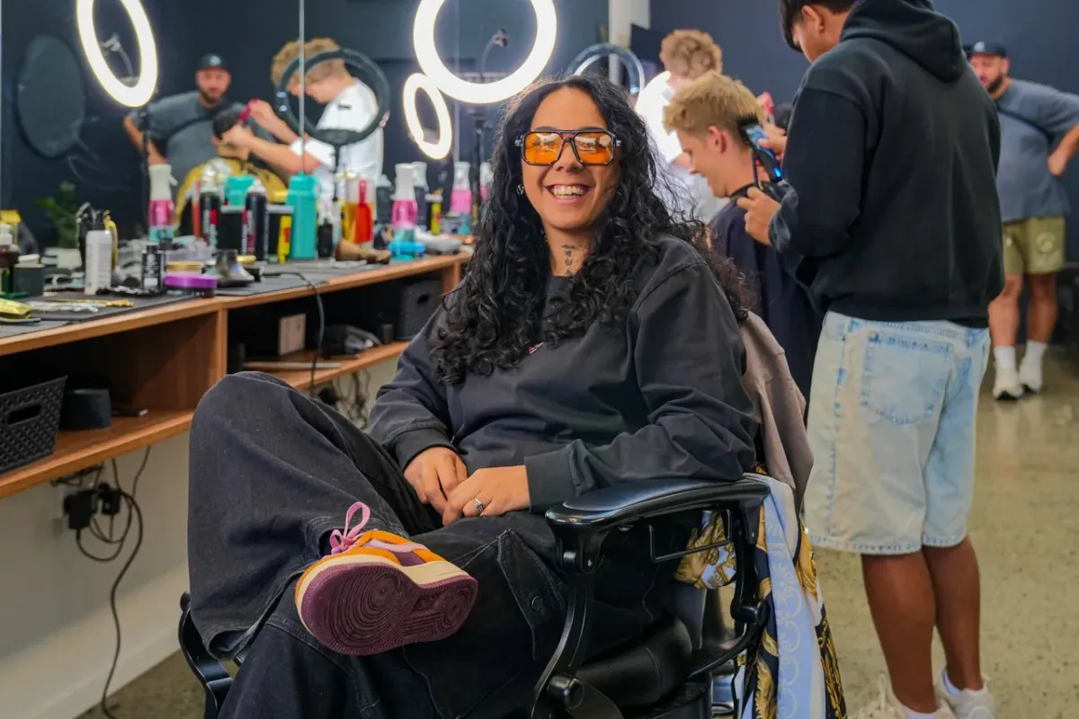 A person smiling in a wheelchair in a busy barbershop