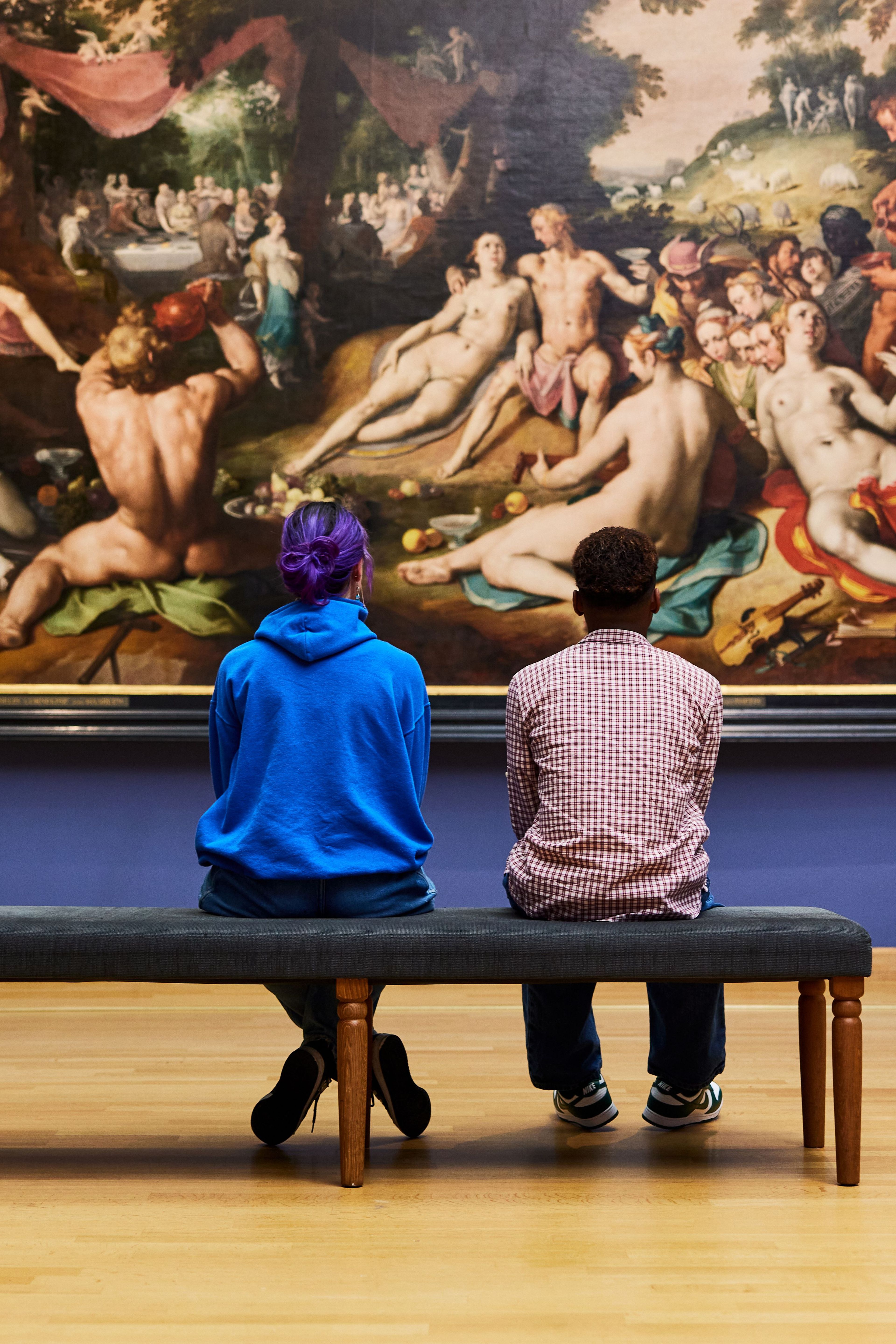 Twee middelbare school leerlingen zitten op een bankje en kijken naar een schilderij.