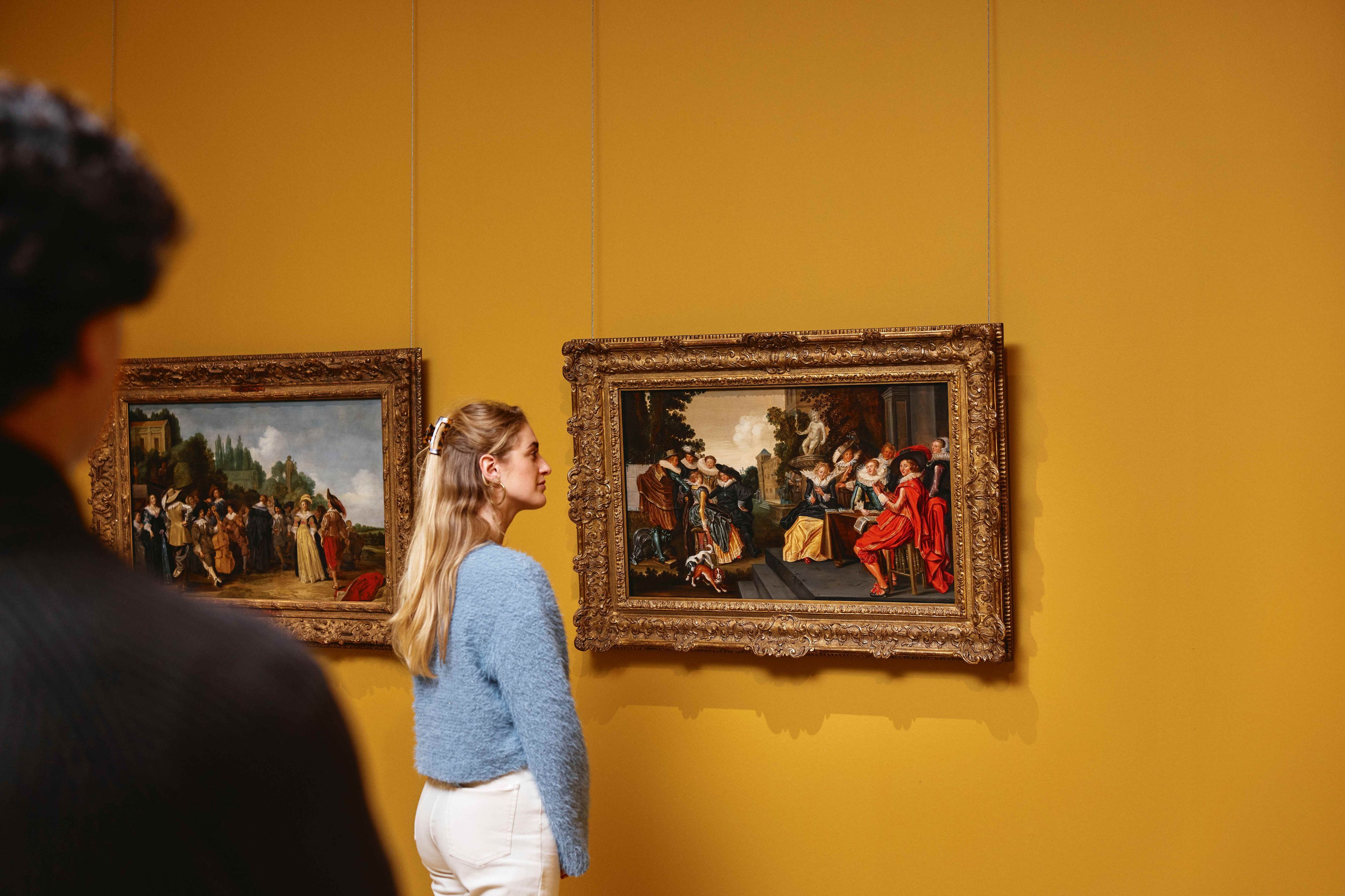 Vrouwelijke bezoeker bekijkt schilderij van Dirck Hals.