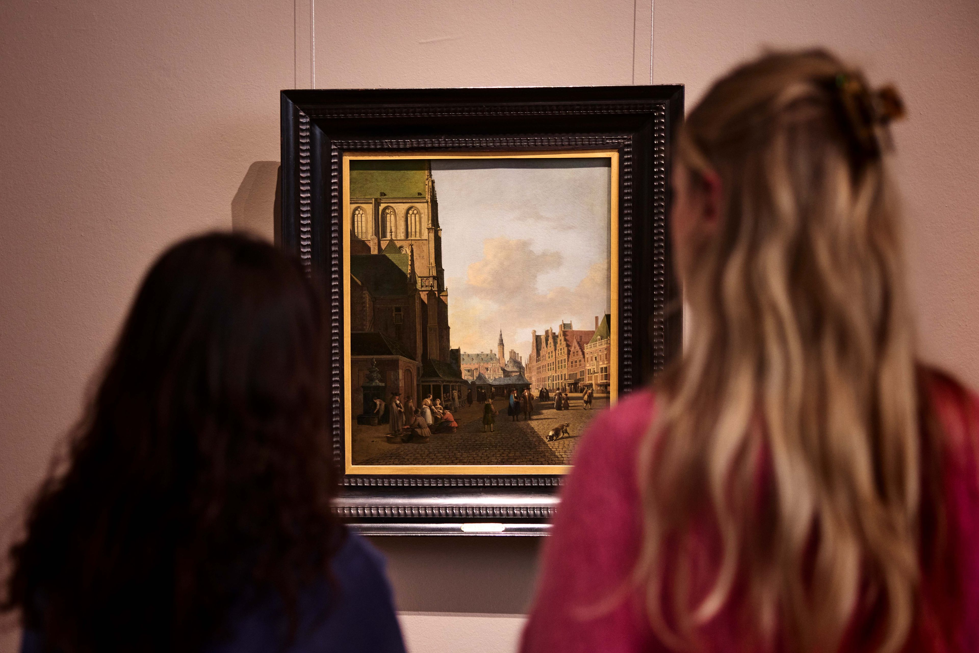 Twee vrouwelijke bezoekers kijken naar een kunstwerk over Haarlem van Berckheyde.
