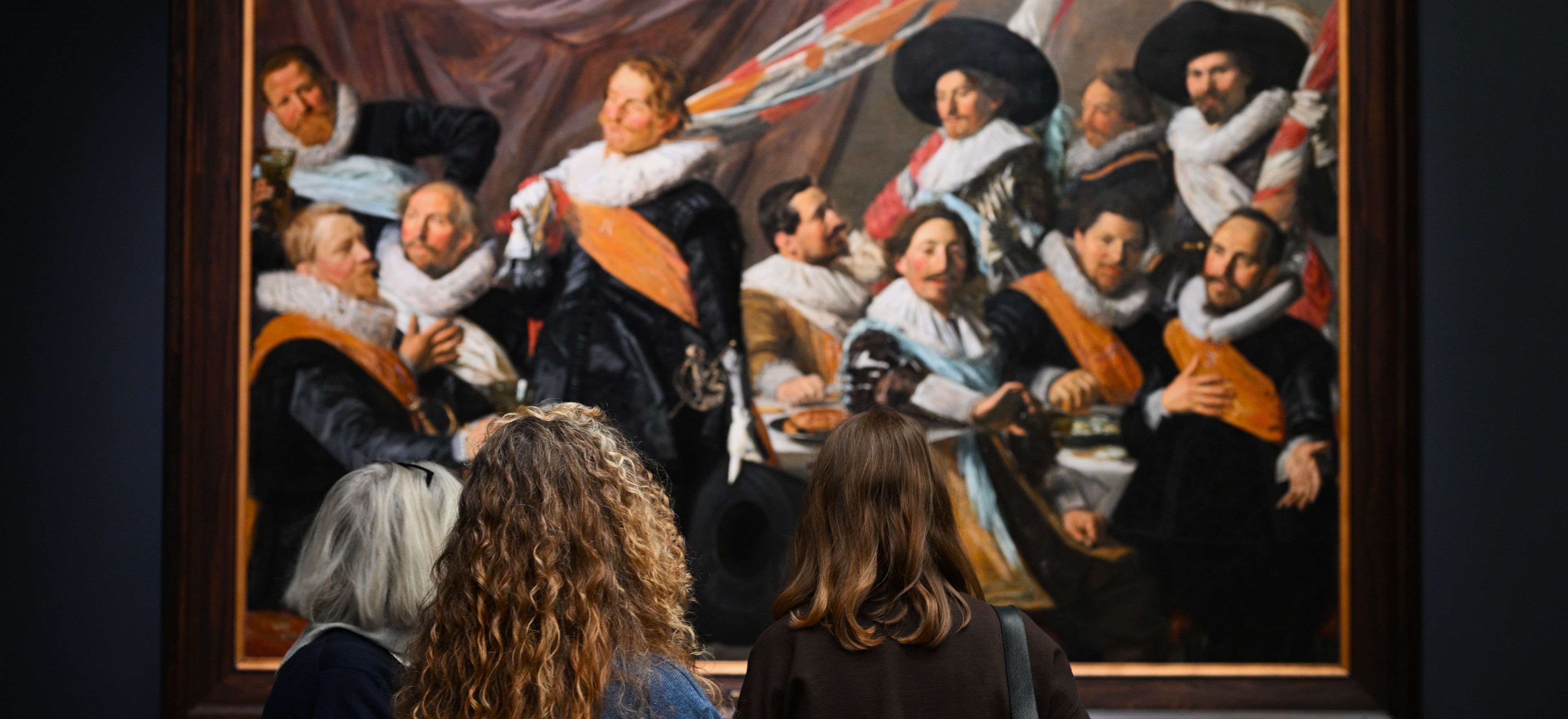 Drie vrouwelijke bezoekers bekijken een van de schuttersstukken van Frans Hals in het Frans Hals Museum.