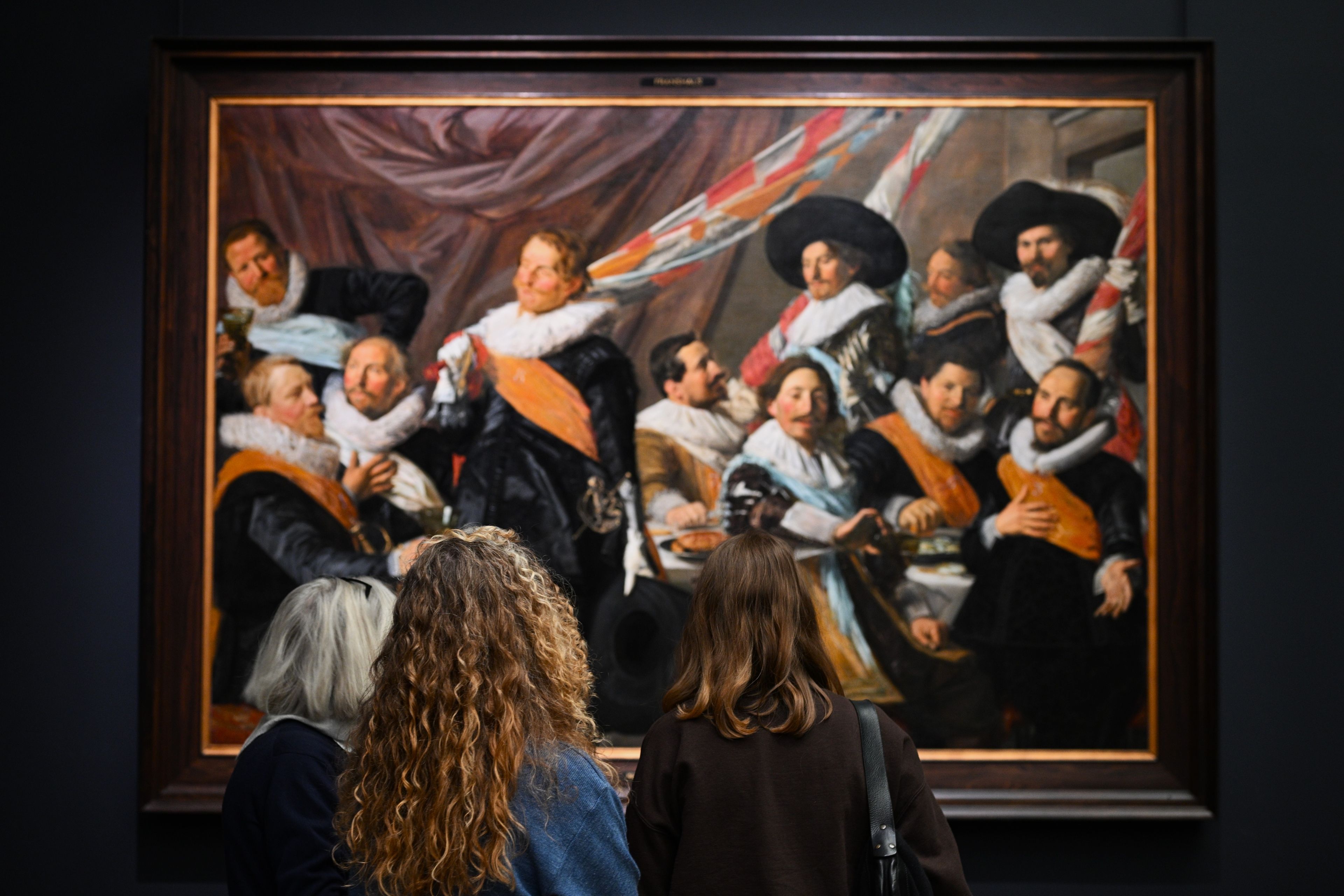 Drie vrouwelijke bezoekers bekijken een van de schuttersstukken van Frans Hals in het Frans Hals Museum.