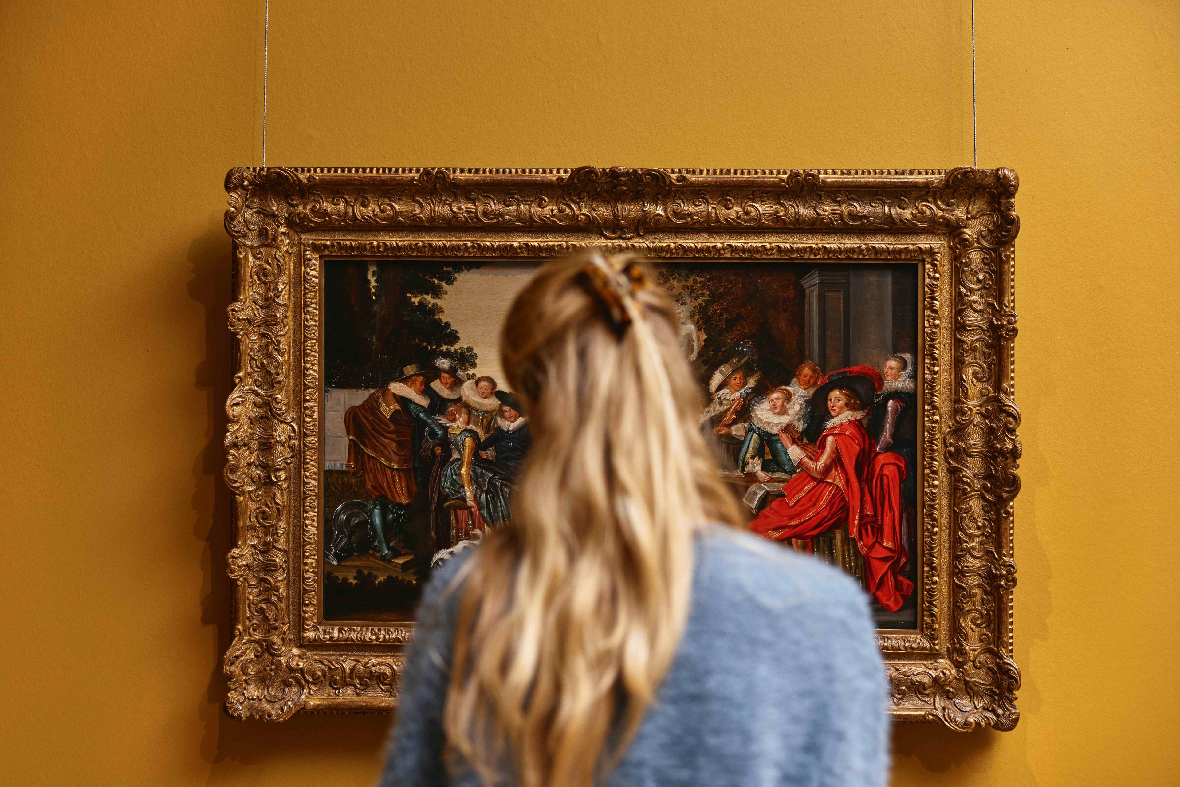 Vrouwelijke bezoeker bekijkt schilderij van Dirck Hals.