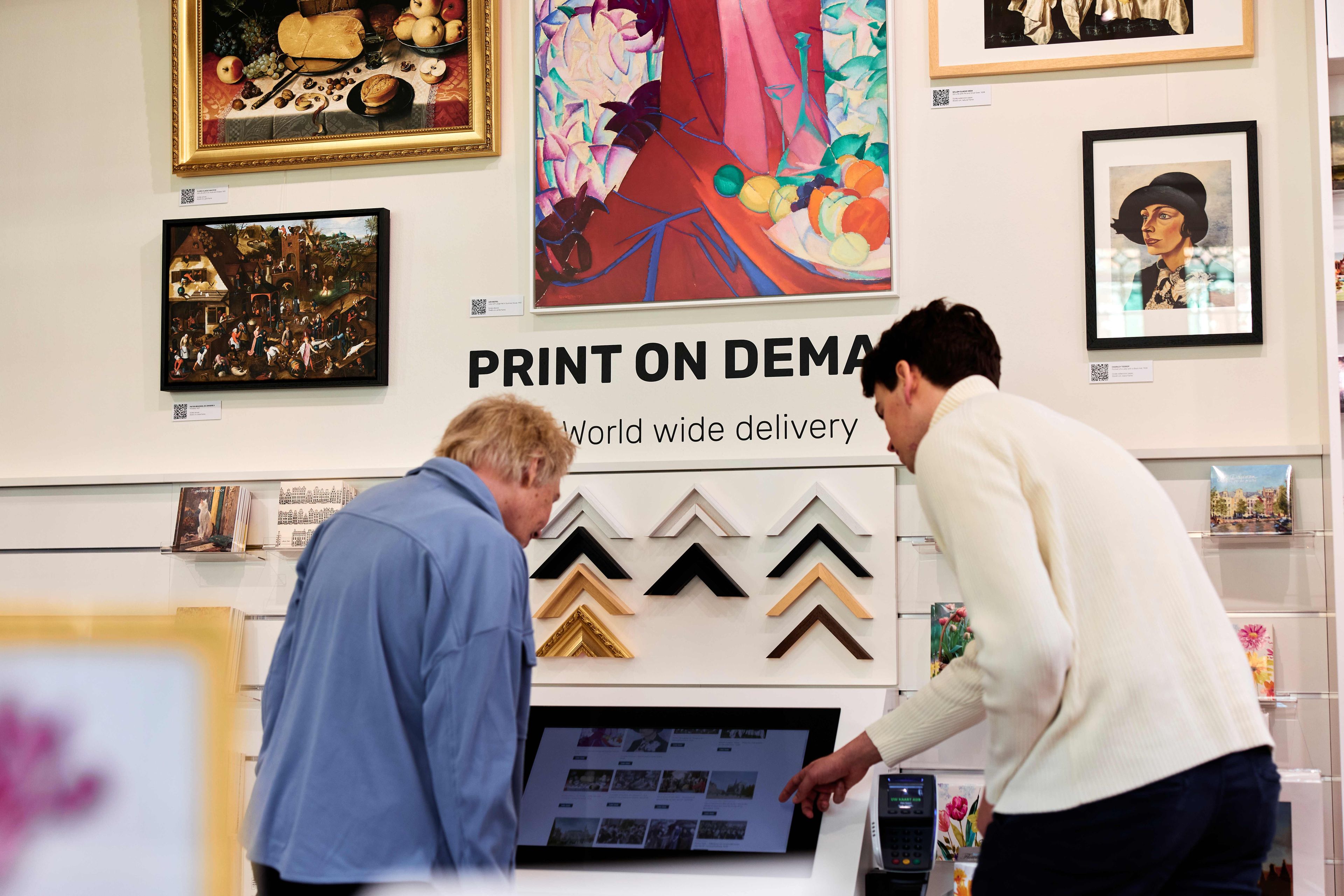 Twee bezoekers bekijken de opties voor Print on Demand in de museumwinkel.