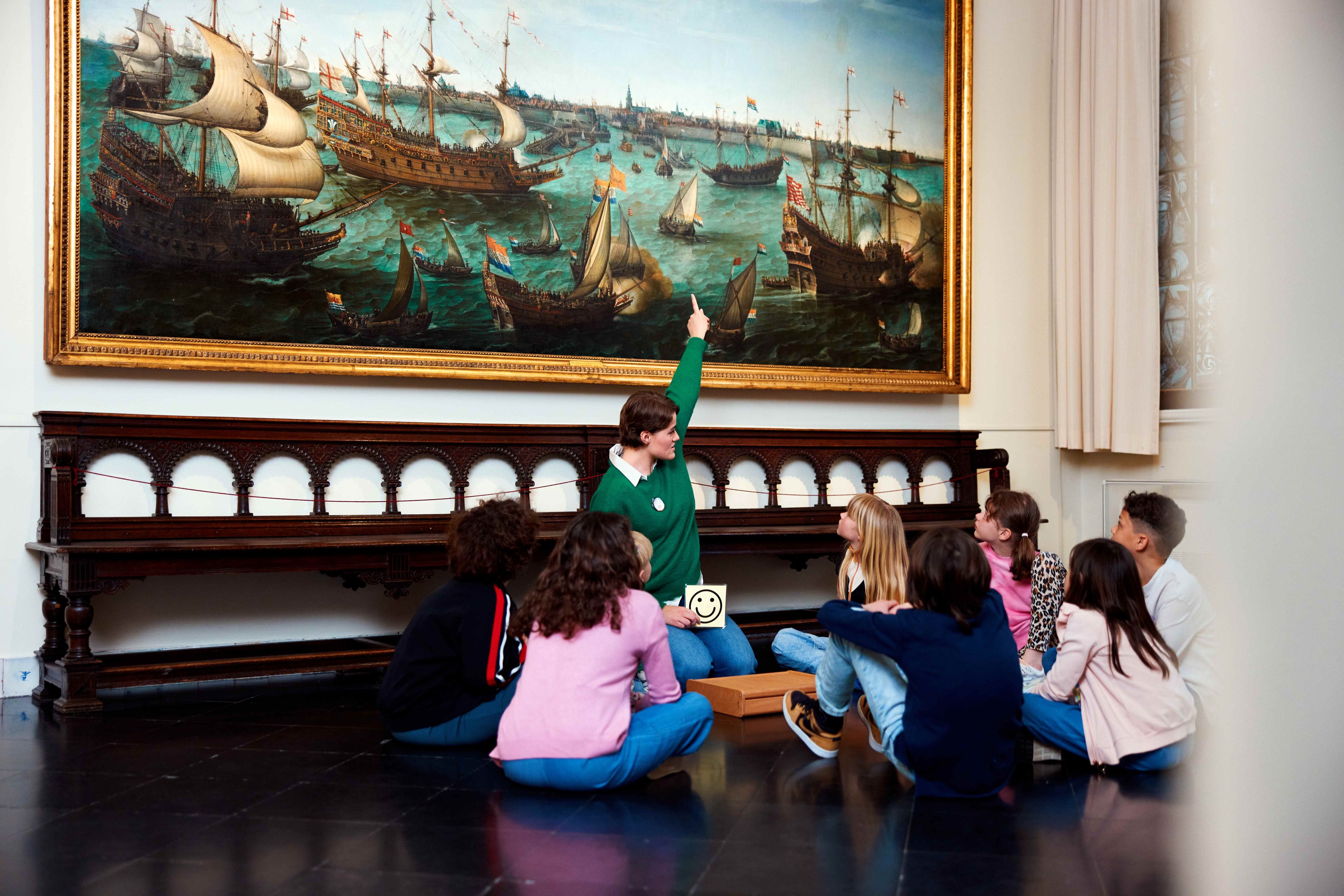 Museumdocent legt meer uit over zeeslag schilderij aan groep leerlingen.