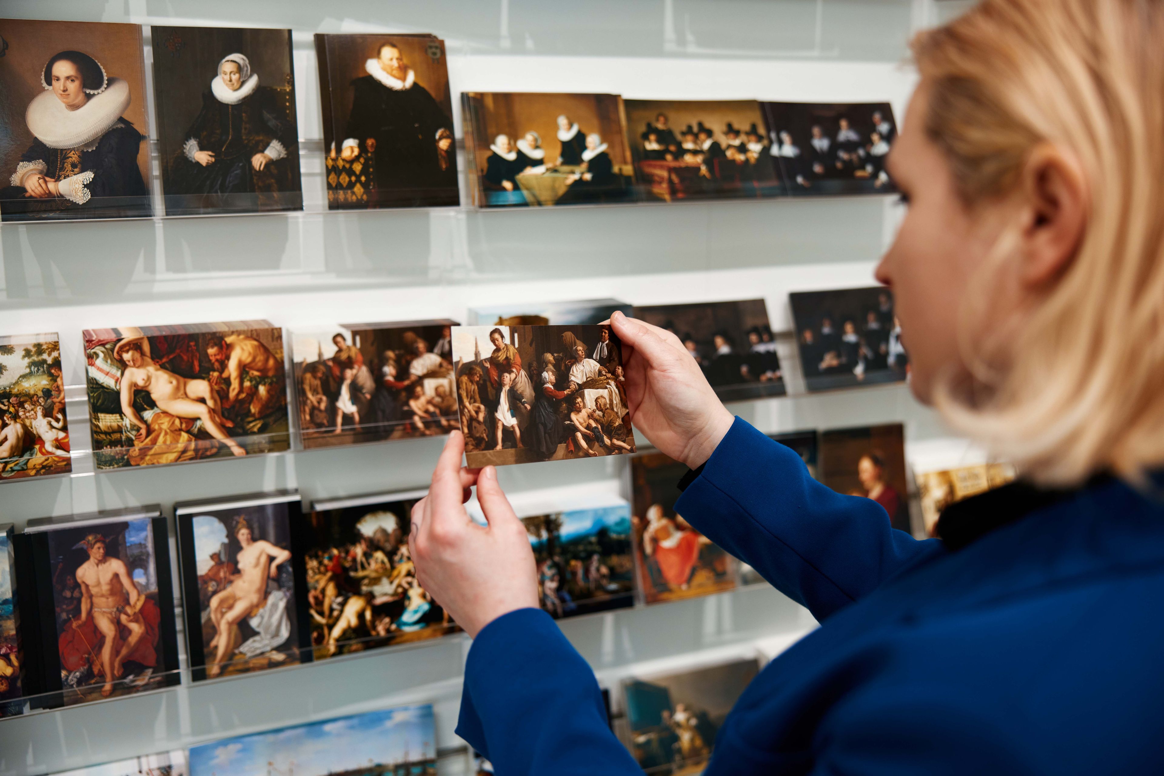 Vrouwelijke bezoeker kijkt naar ansichtkaarten in de museumwinkel van het Frans Hals Museum.