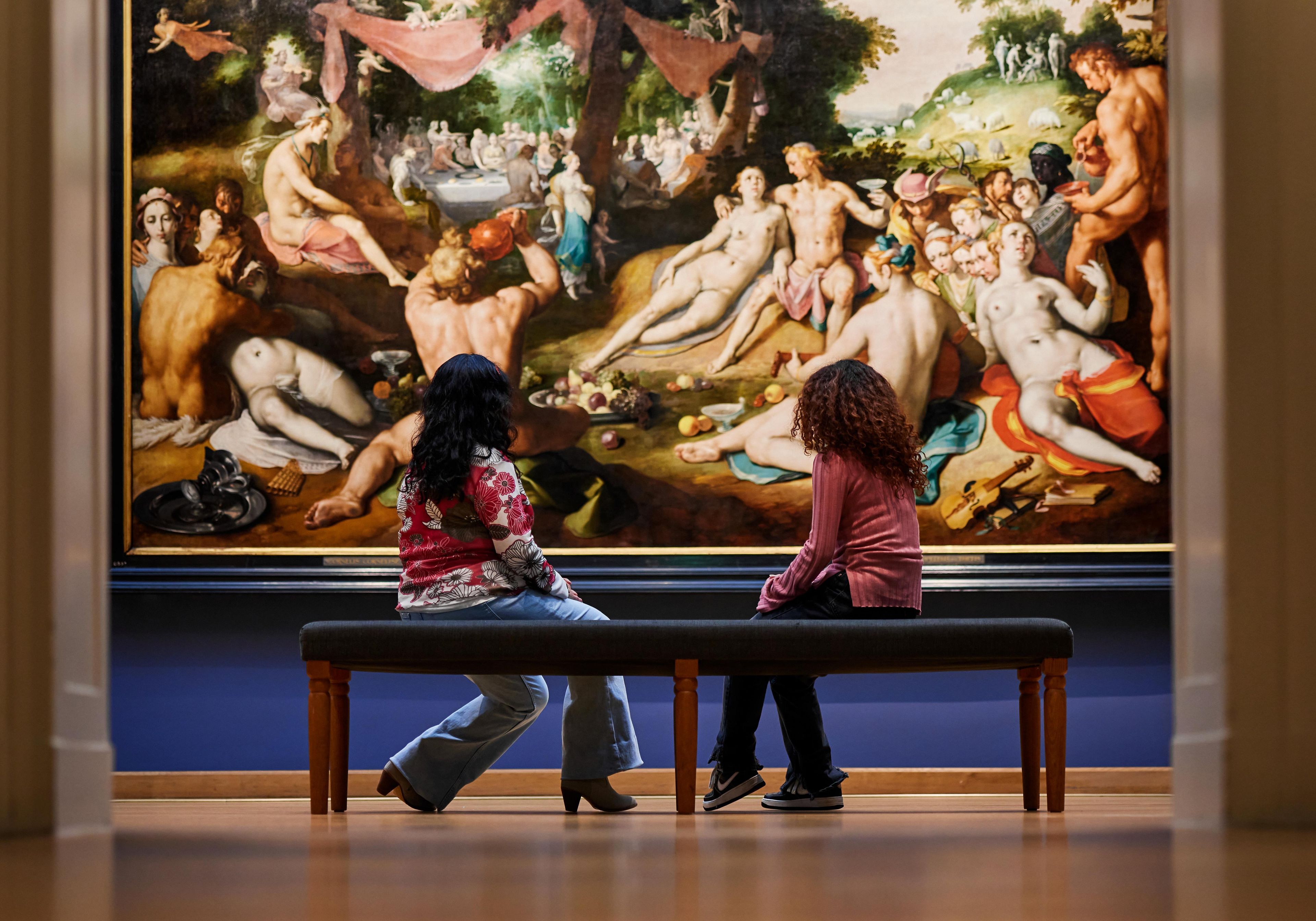 Two visitors on a bench looking at a work of art by Cornelis van Haarlem.