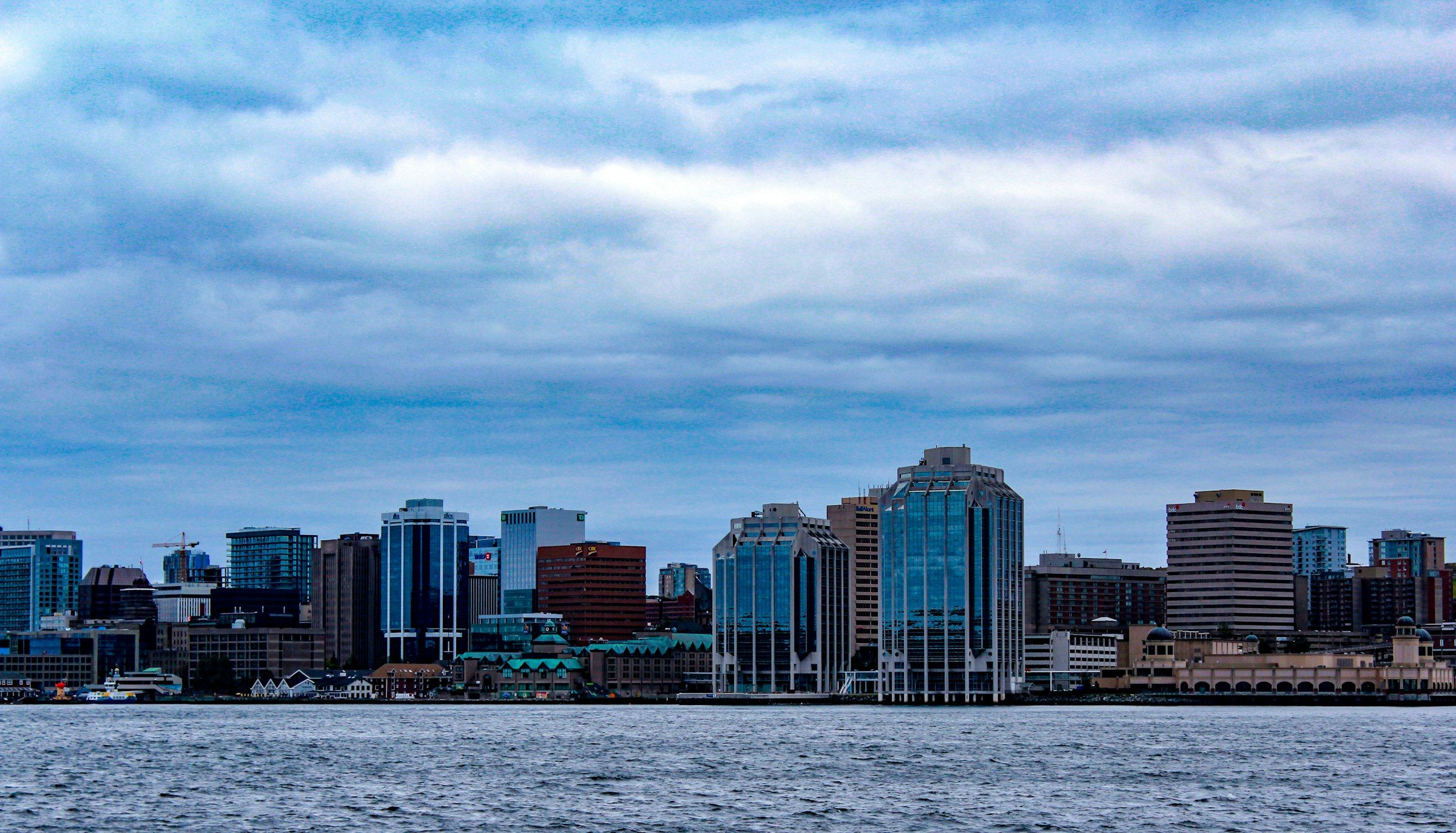 Halifax waterfront with downtown buildings across calm harbour water under a cloudy sky