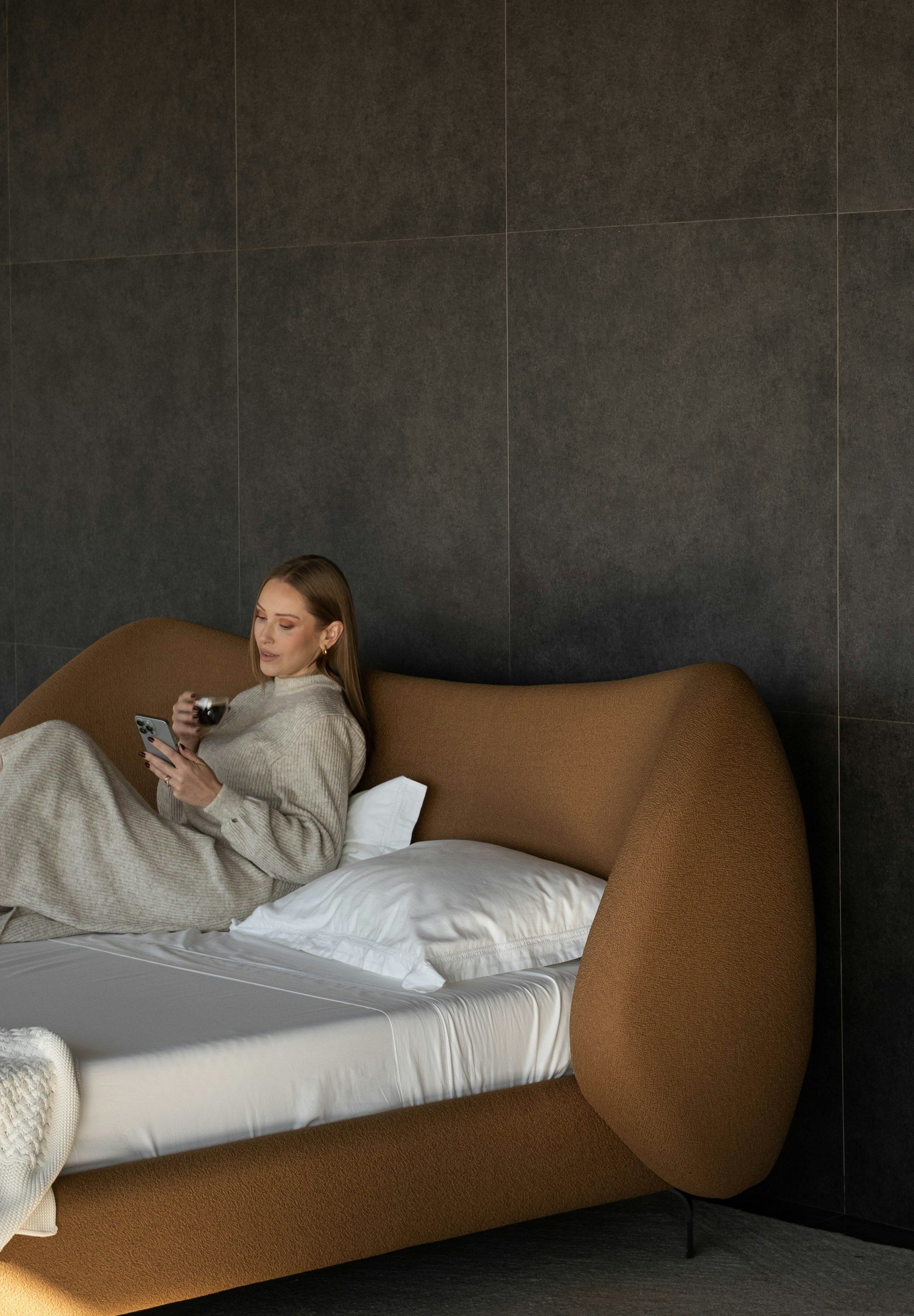 Woman sitting in bed in the morning with a mug of coffee, looking at her phone