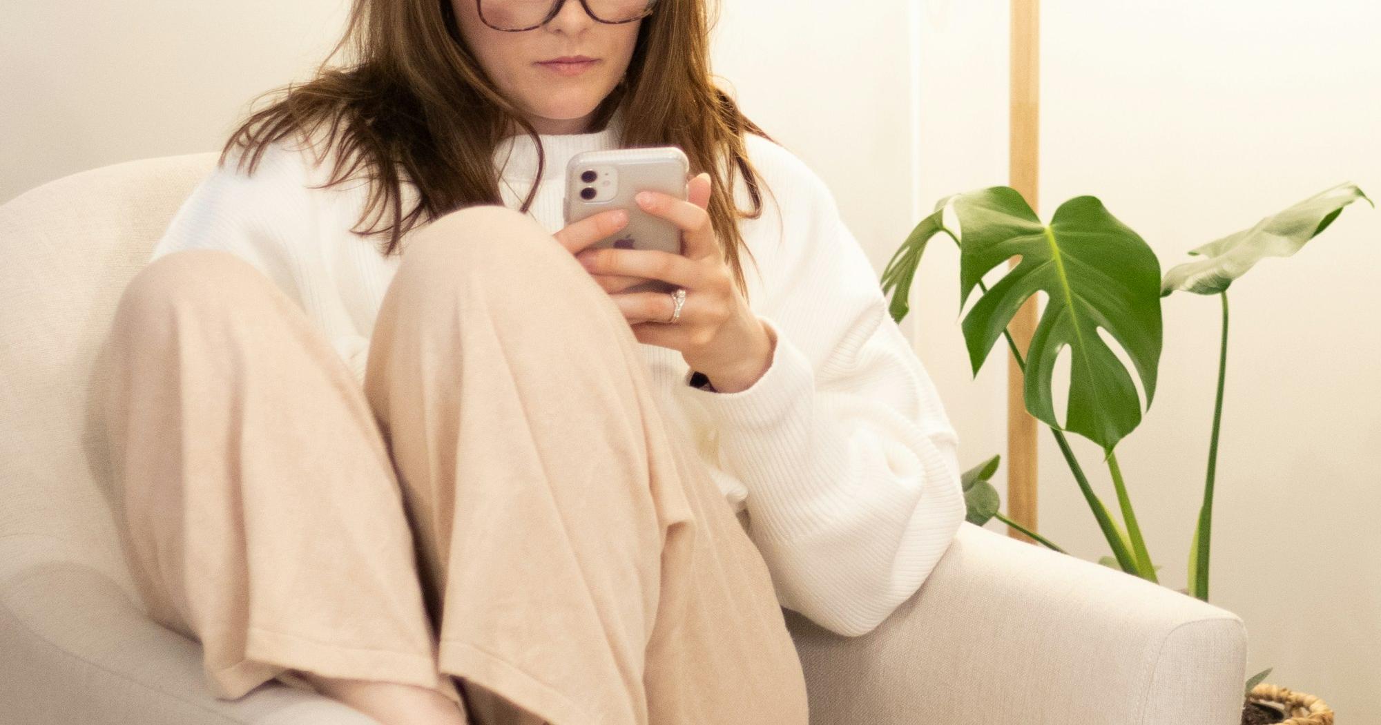 Woman relaxing in a chair at home and reading her phone, with plants in the background