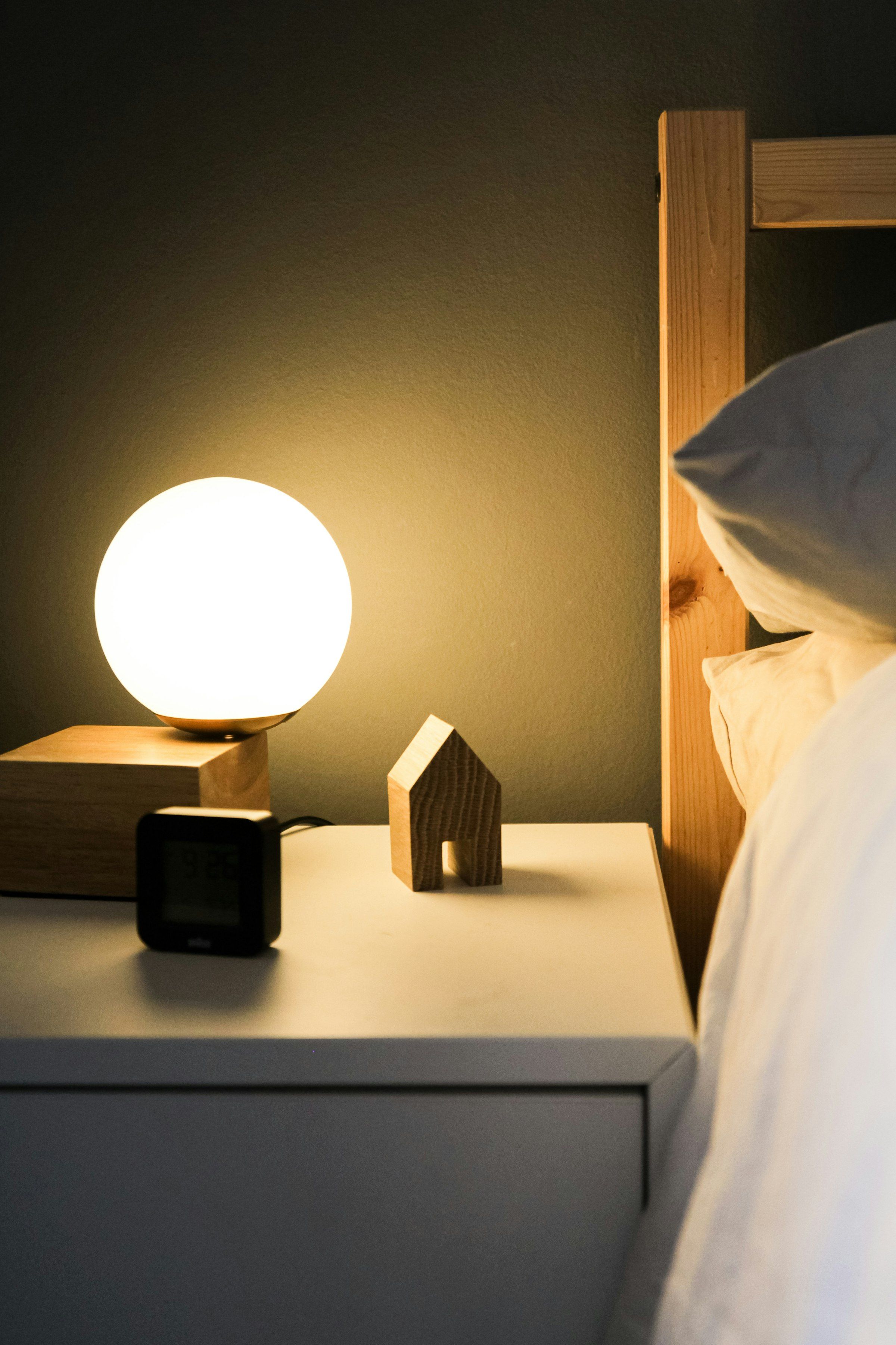 Softly glowing globe lamp, small wooden house and digital clock on a bedside nightstand at night